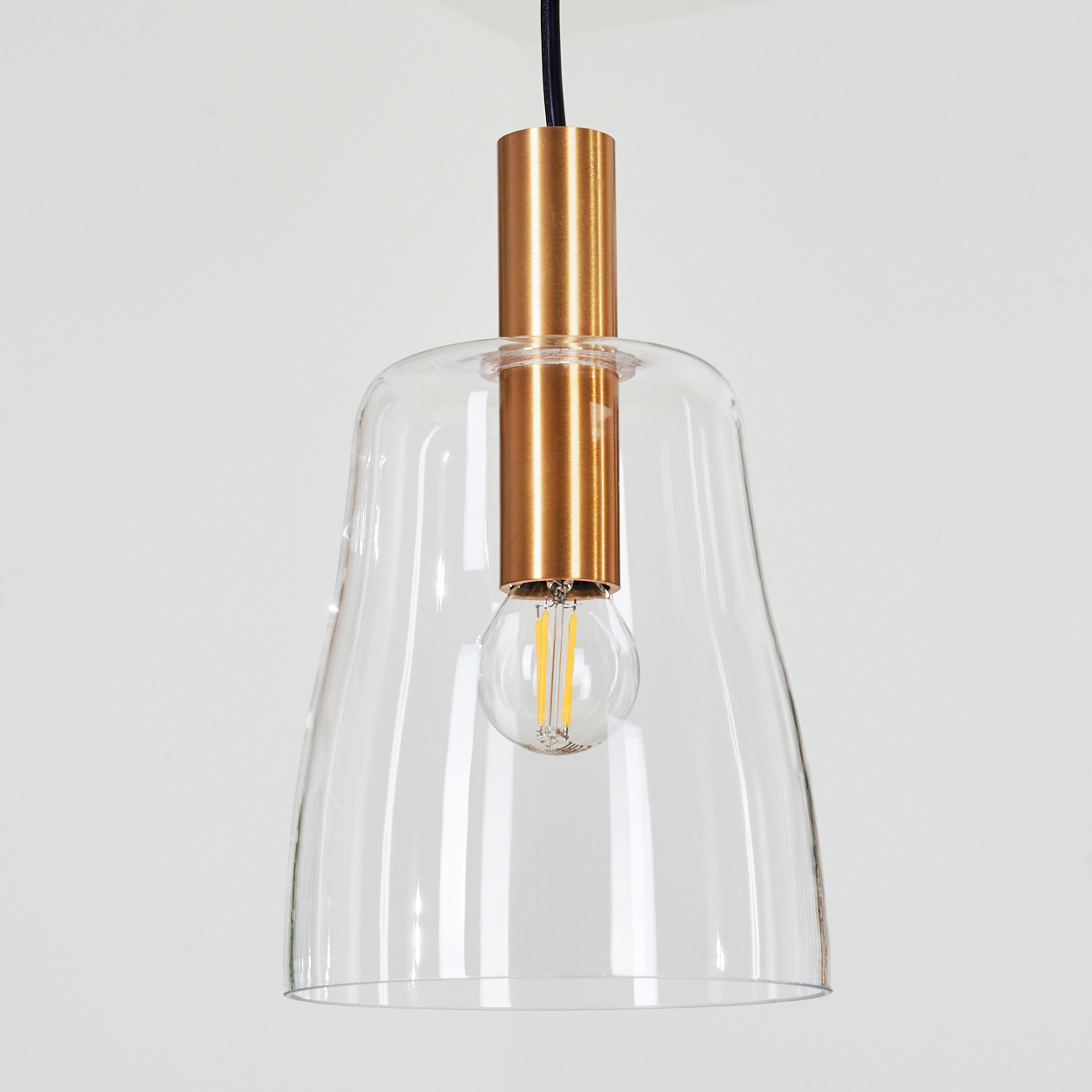 Eine moderne Pendelleuchte mit klarem Glasschirm, Messingfarbenen Metallakzenten und einer sichtbaren Glühbirne vor weißem Hintergrund.