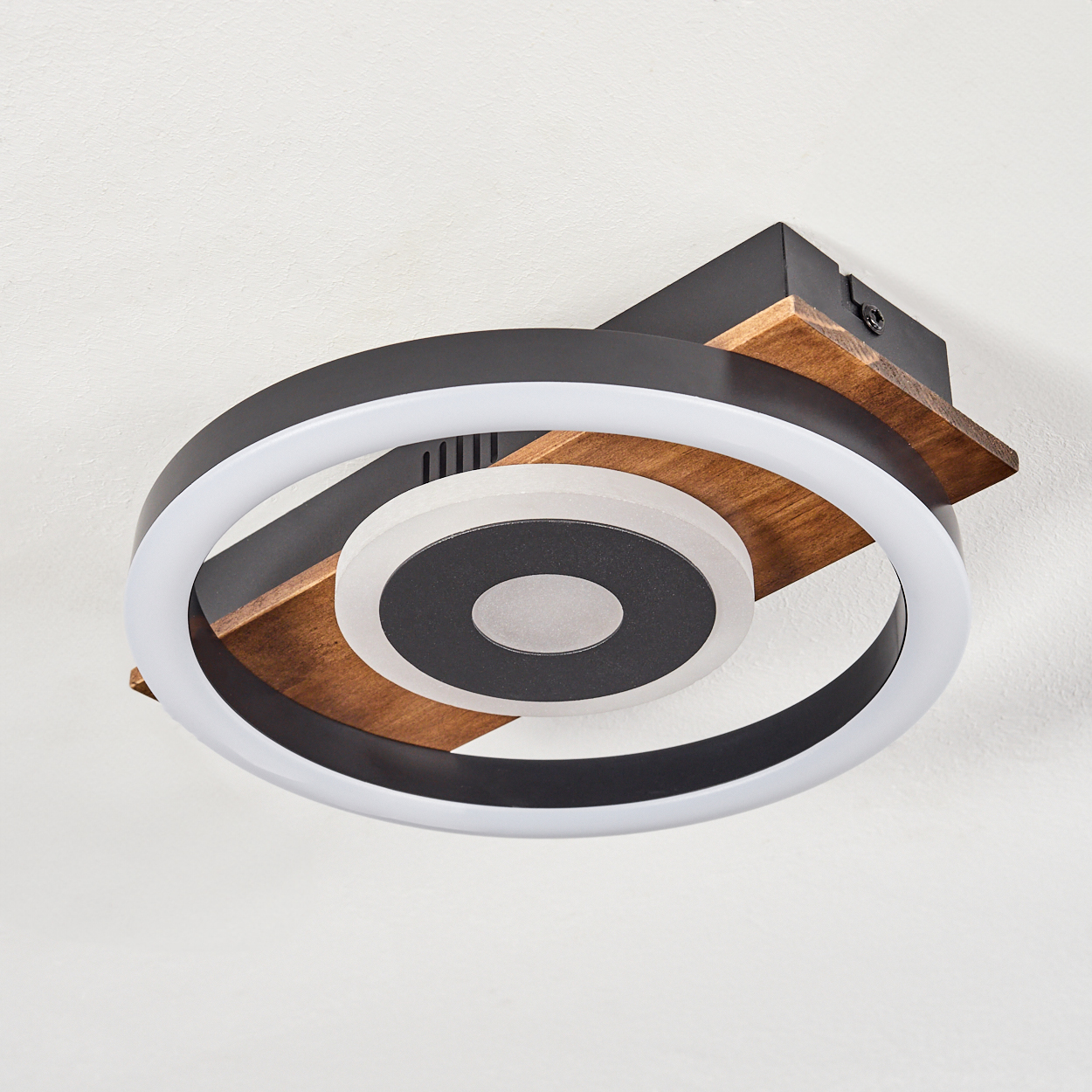 Eine moderne Deckenleuchte. Sie hat ein kreisförmiges Design mit weißen und schwarzen Ringen, Holz und einem weißen Deckenhintergrund.