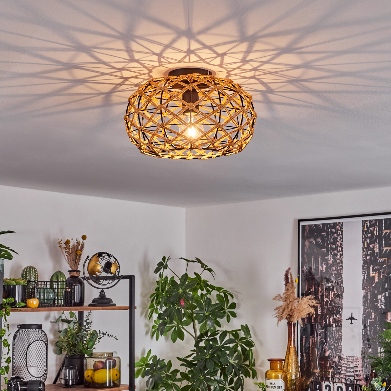 Eine gewebte Leuchte hängt von der Decke. Darunter steht ein Regal mit Pflanzen und Dekoration. Ein Stadtbilddruck an der Wand.