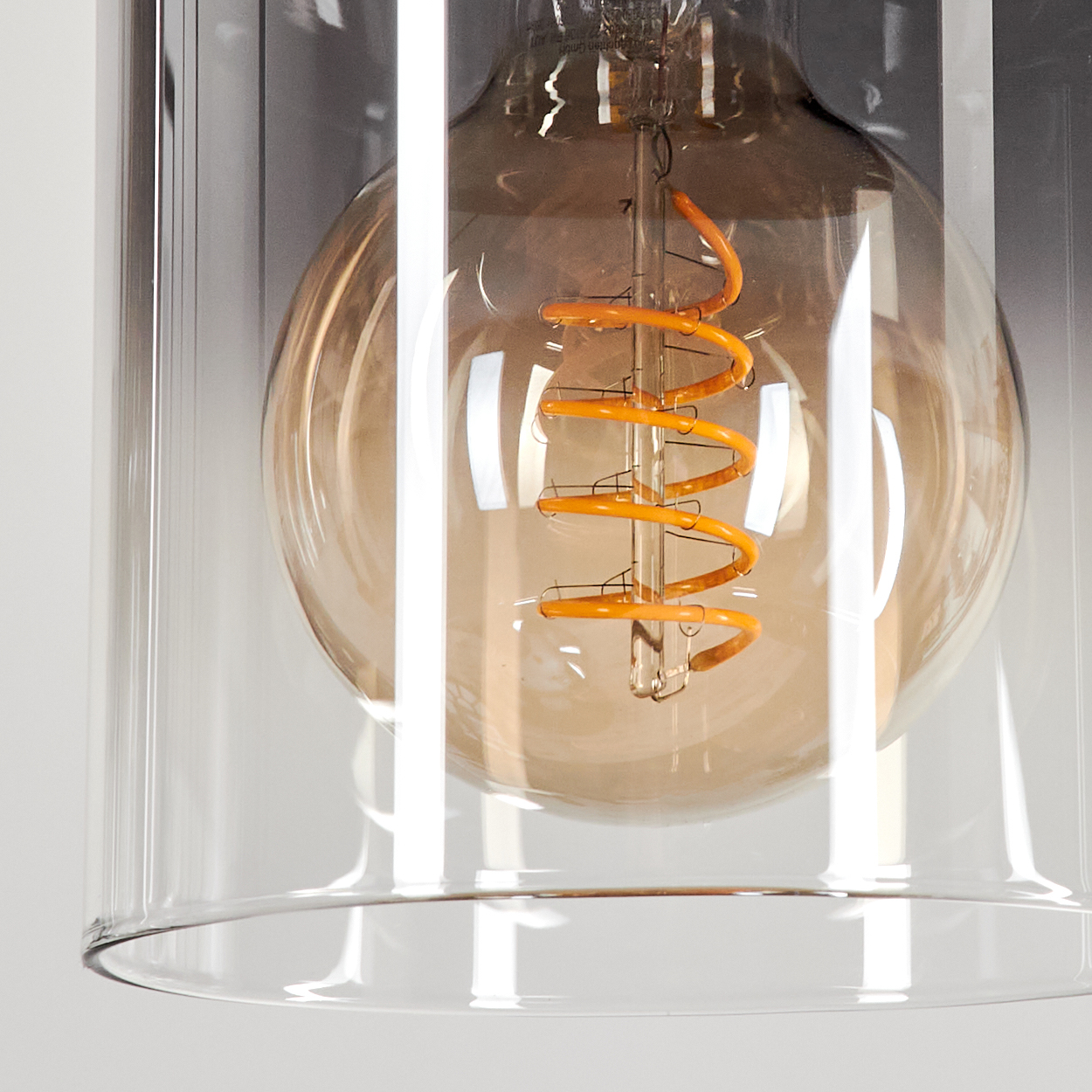 Nahaufnahme einer Glühbirne. Die Glühbirne hat einen Spiralglühfaden und ist von einem Glaszylinder umgeben. Der Hintergrund ist verschwommen.