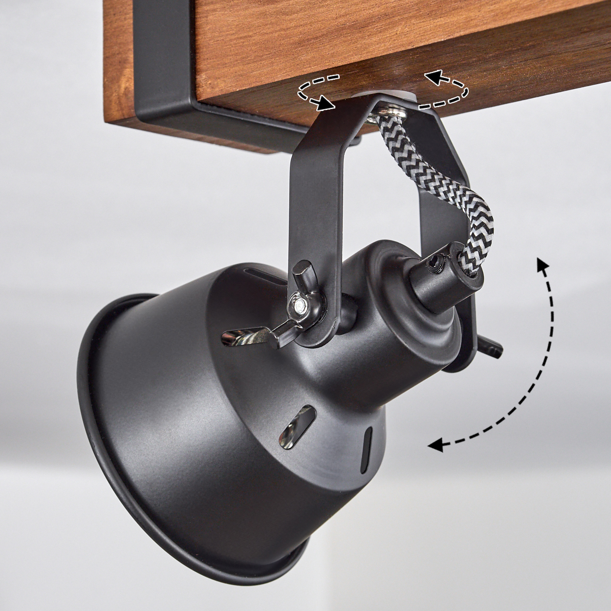 Ein schwarzer Strahler ist an einem Holzbalken montiert. Ein schwarz-weiß geflochtenes Kabel verbindet das Licht. Das Licht ist einstellbar.