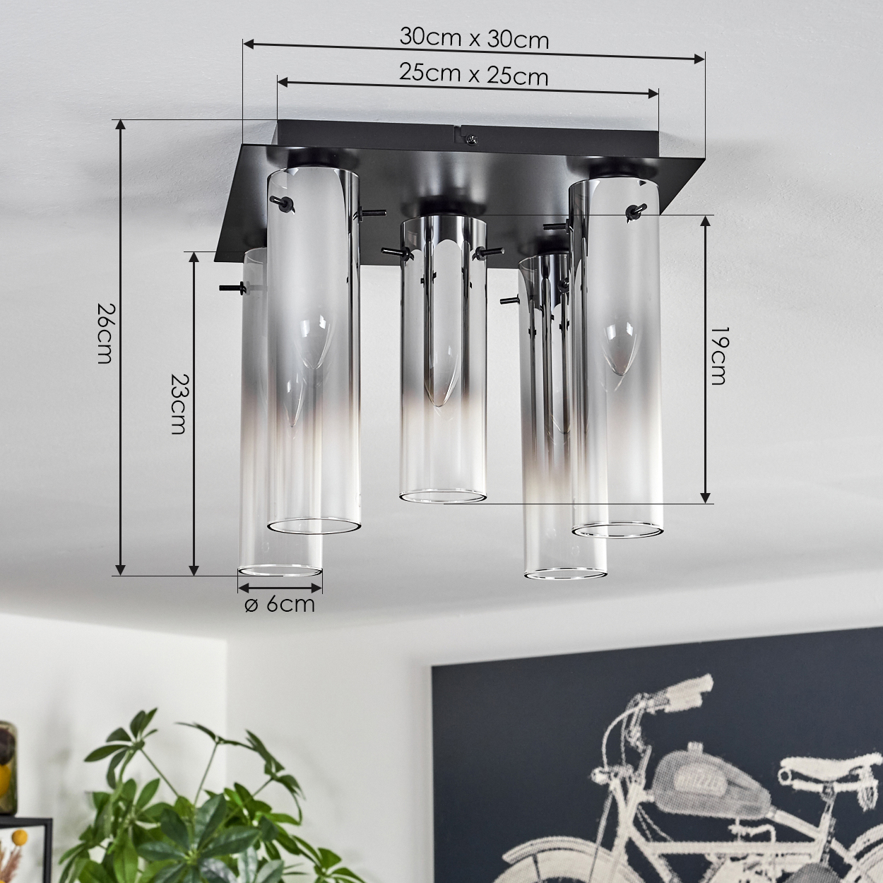 Eine Deckenleuchte mit Glaszylindern, Maße sind angegeben. Ein Gemälde eines Motorrads und eine Pflanze befinden sich im Hintergrund.