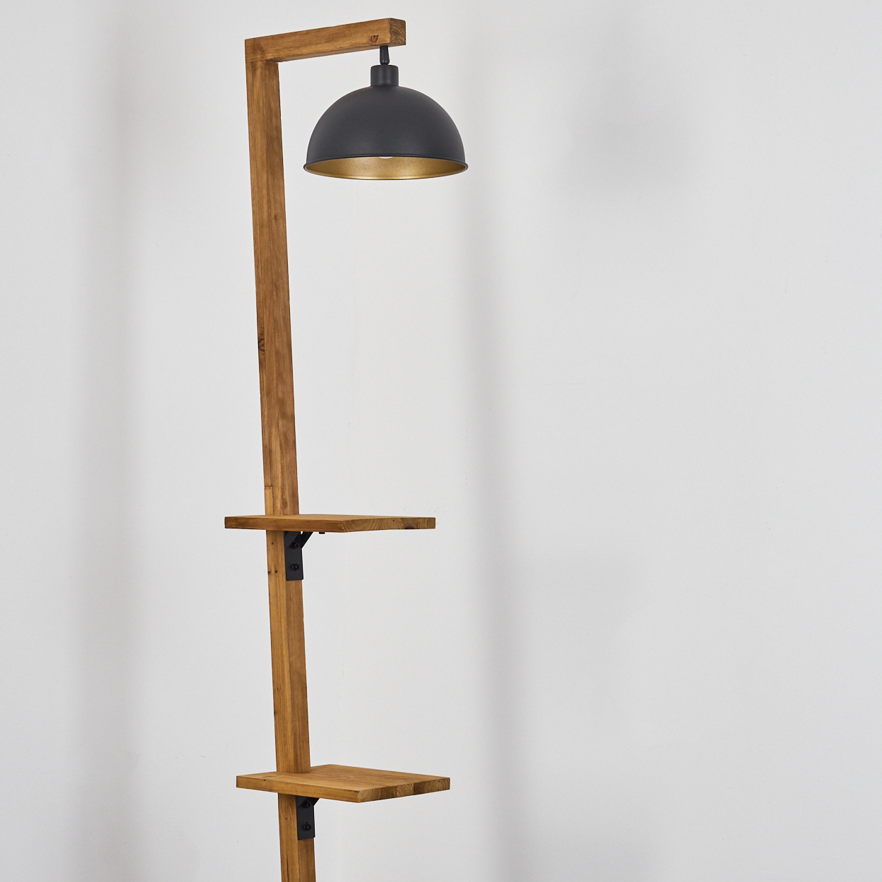 Stehlampe aus Holz mit schwarzem Lampenschirm und zwei Ablagen. Der Hintergrund ist eine weiße Wand.