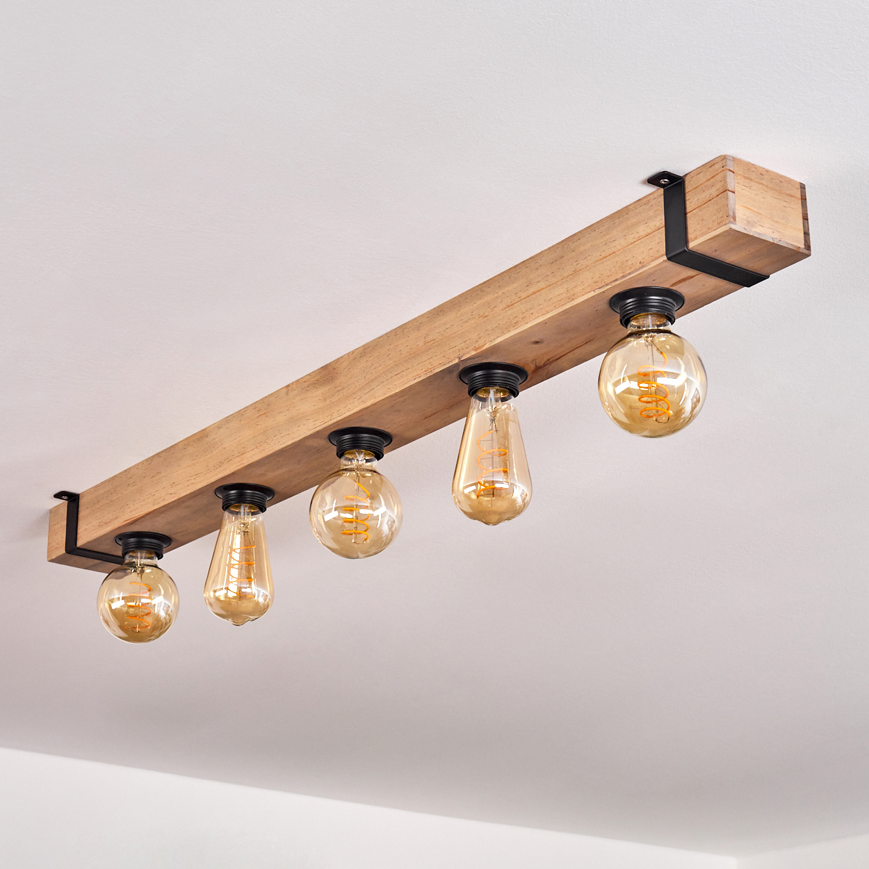 Eine Deckenleuchte aus Holzbalken mit fünf Edison-Glühbirnen. Der Balken ist mit schwarzen Metallwinkeln an der Decke befestigt.