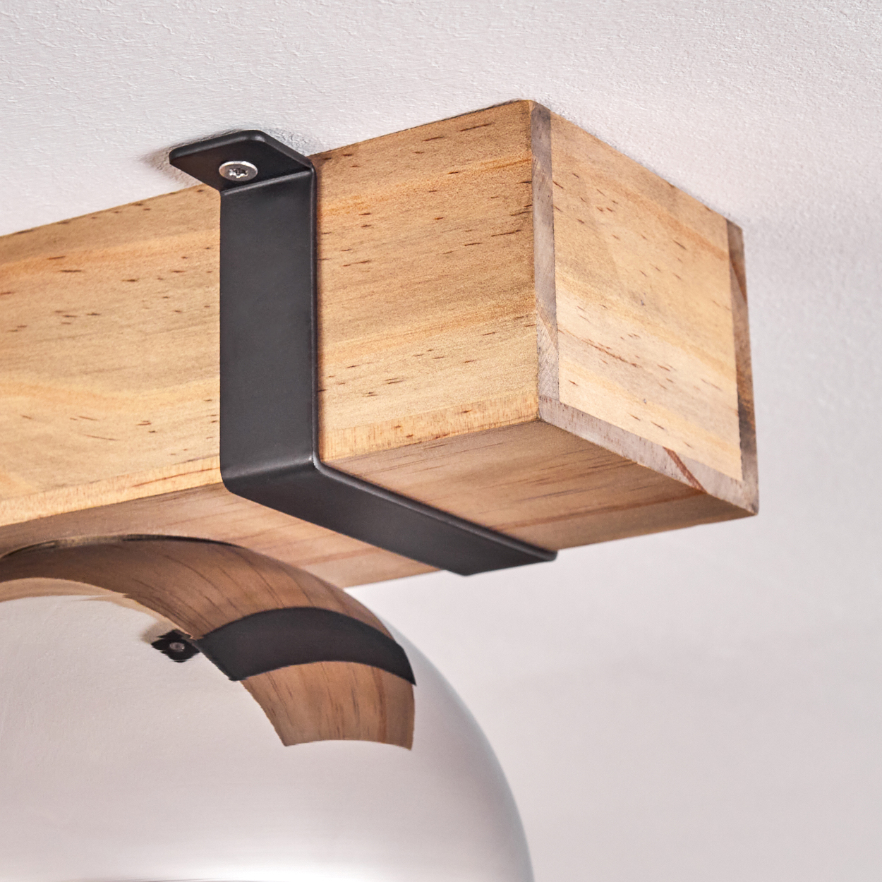 Ein Holzbalken wird von schwarzen Metallhalterungen an einer weißen Decke gehalten. Unter dem Balken befindet sich eine silberne Lampe.