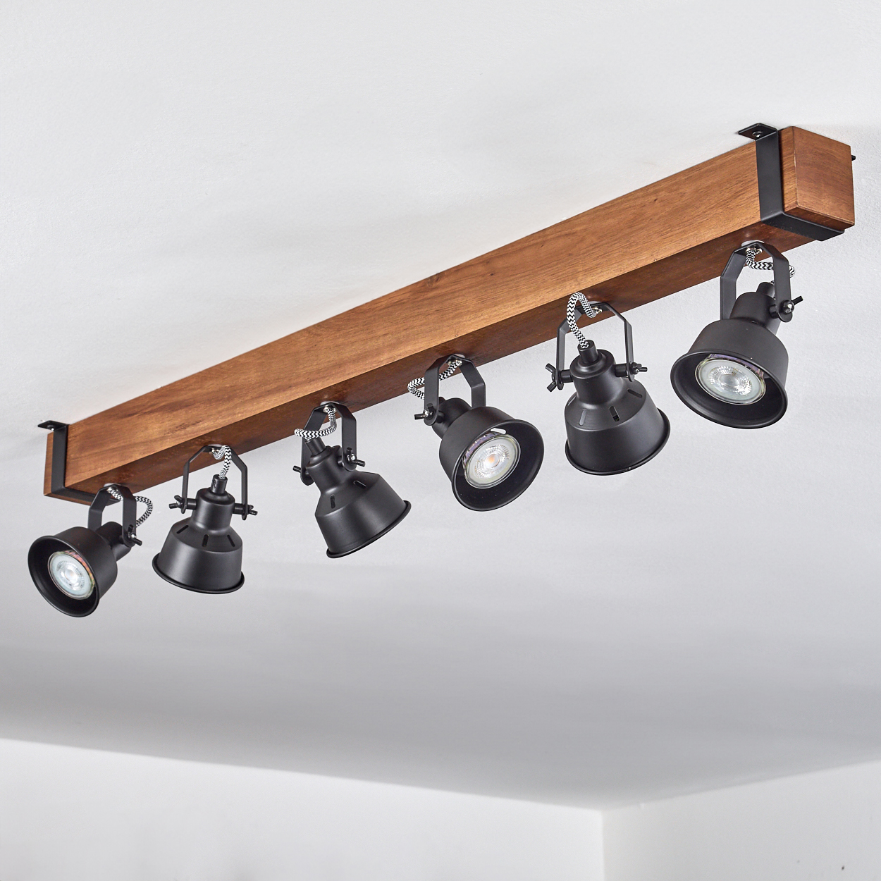 Ein Holzbalken mit sechs schwarzen Strahlern. Die Lichter sind nach unten geneigt. Der Hintergrund ist eine weiße Decke.