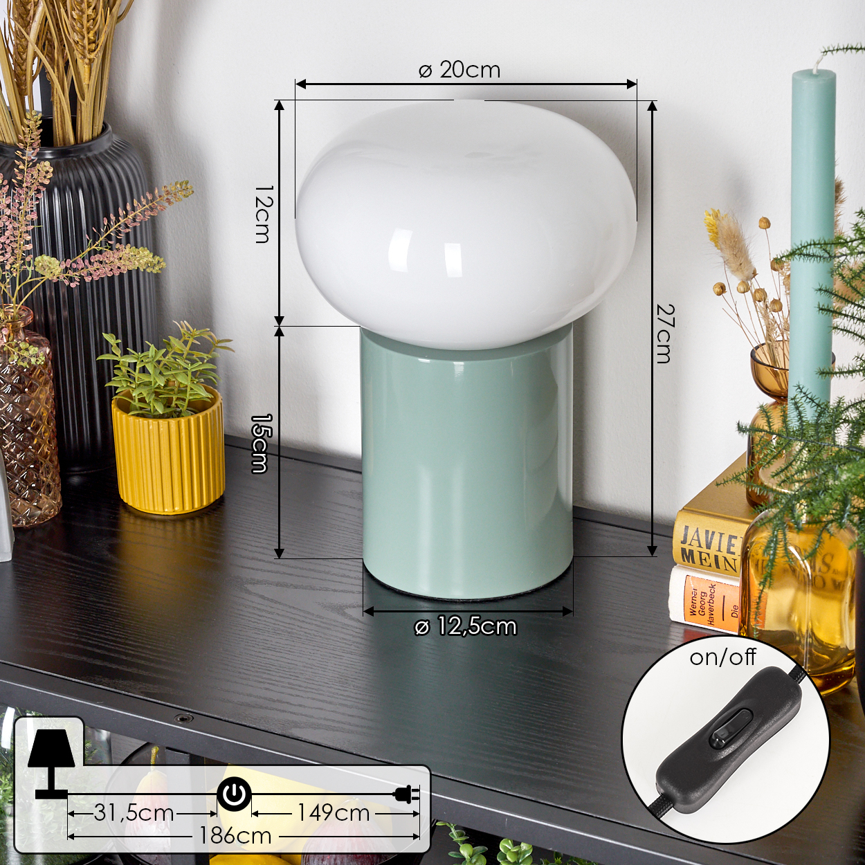 Eine pilzförmige Lampe mit weißem Oberteil und grünem Sockel steht auf einem schwarzen Regal. Weitere Objekte sind Kerzen und Dekorationsartikel.
