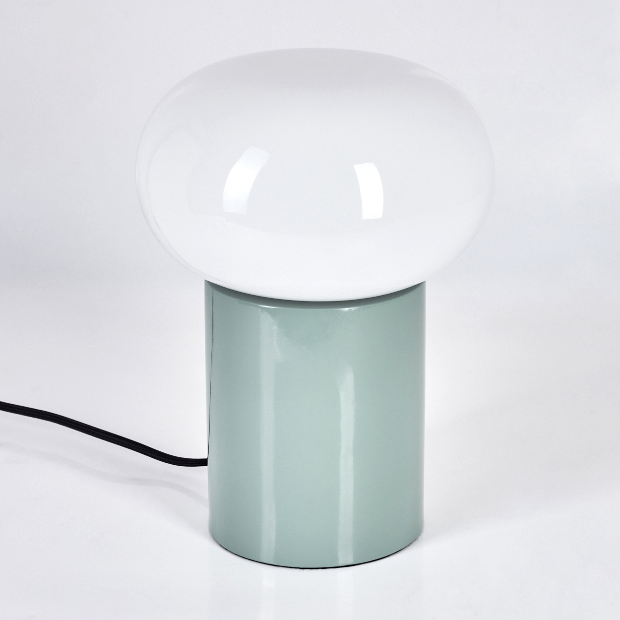 Eine moderne Lampe mit weißem Kugelschirm auf einem hellgrünen zylindrischen Sockel. Ein schwarzes Kabel geht von der Basis vor weißem Hintergrund aus.