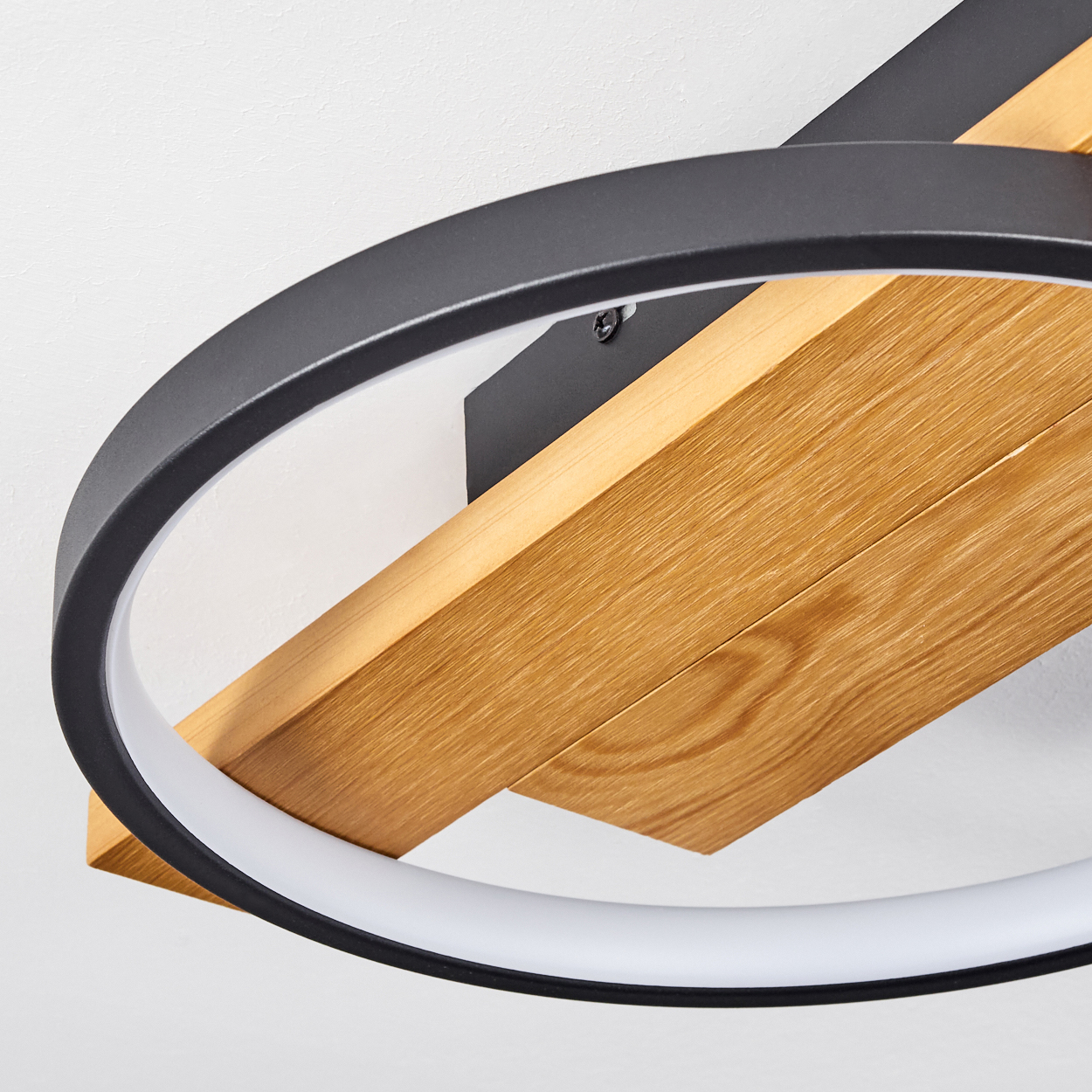 Nahaufnahme einer modernen Deckenleuchte. Sie hat einen schwarzen Ring und Holzbalken vor einer weißen Decke.