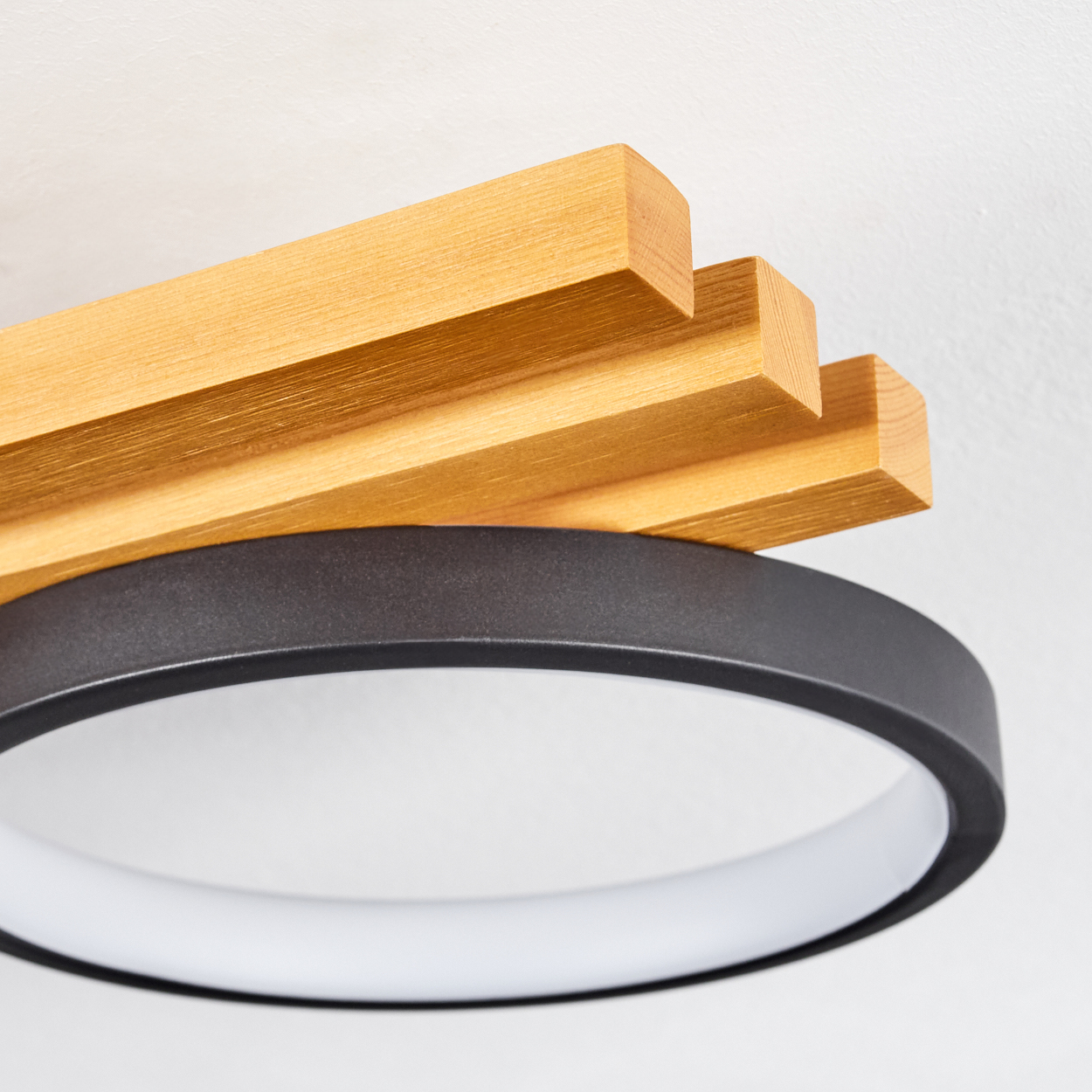 Moderne Deckenleuchte. Holzlatten über einem schwarzen Ring, mit einem weißen, leuchtenden Innenring. Weißer Hintergrund.