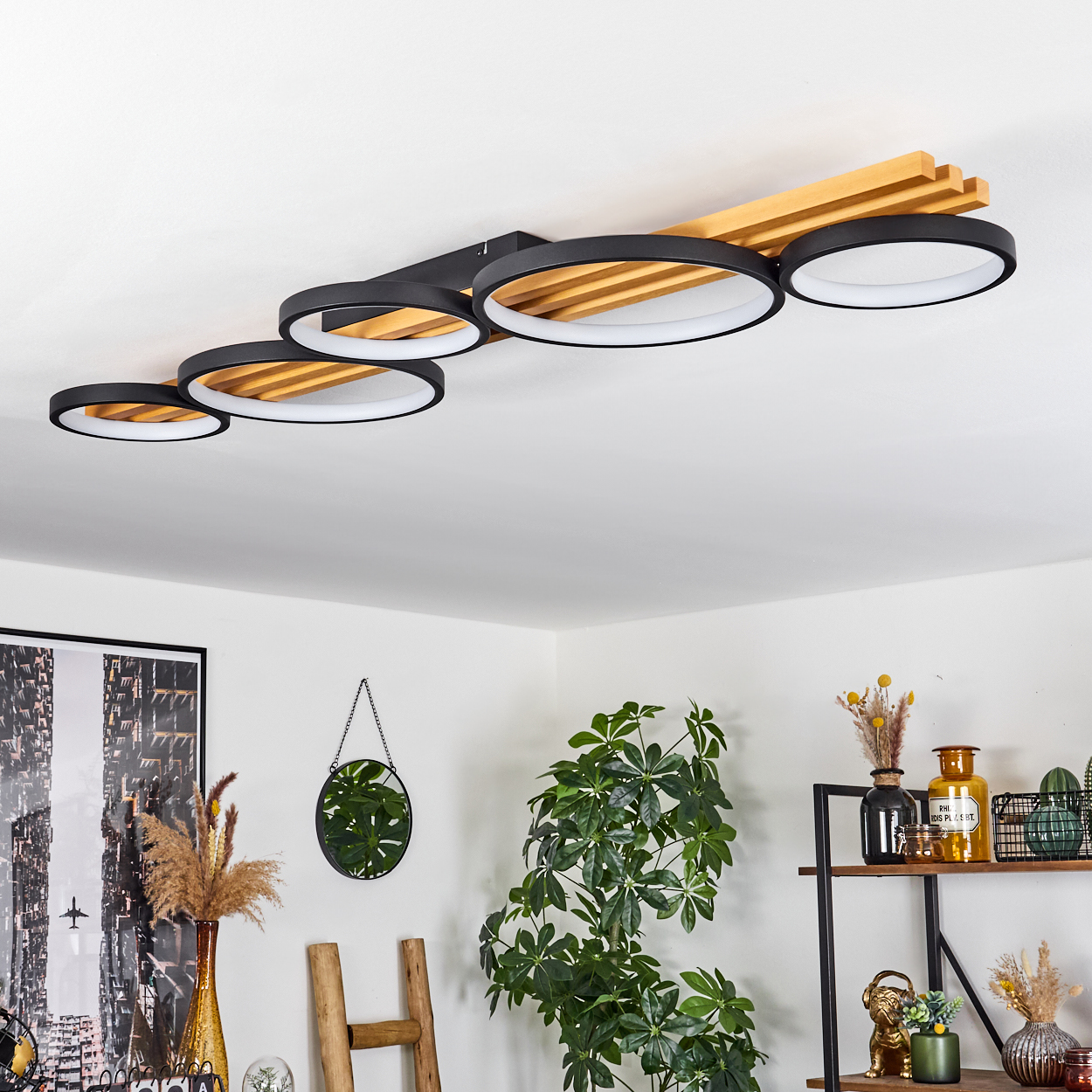Moderne Deckenleuchte mit schwarzen Ringen und Holzakzenten. Pflanzen, Spiegel und Dekoration in einem hellen Raum.