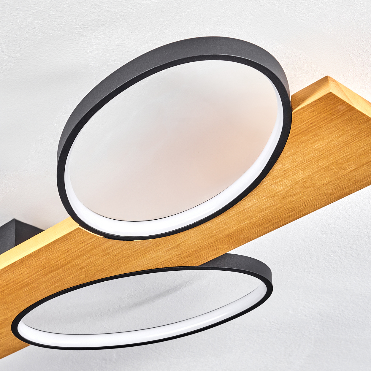 Moderne Deckenleuchte mit zwei kreisförmigen Lichtern. Die Leuchten haben schwarze Ränder und sitzen auf einem Holzbalken an einer weißen Decke.
