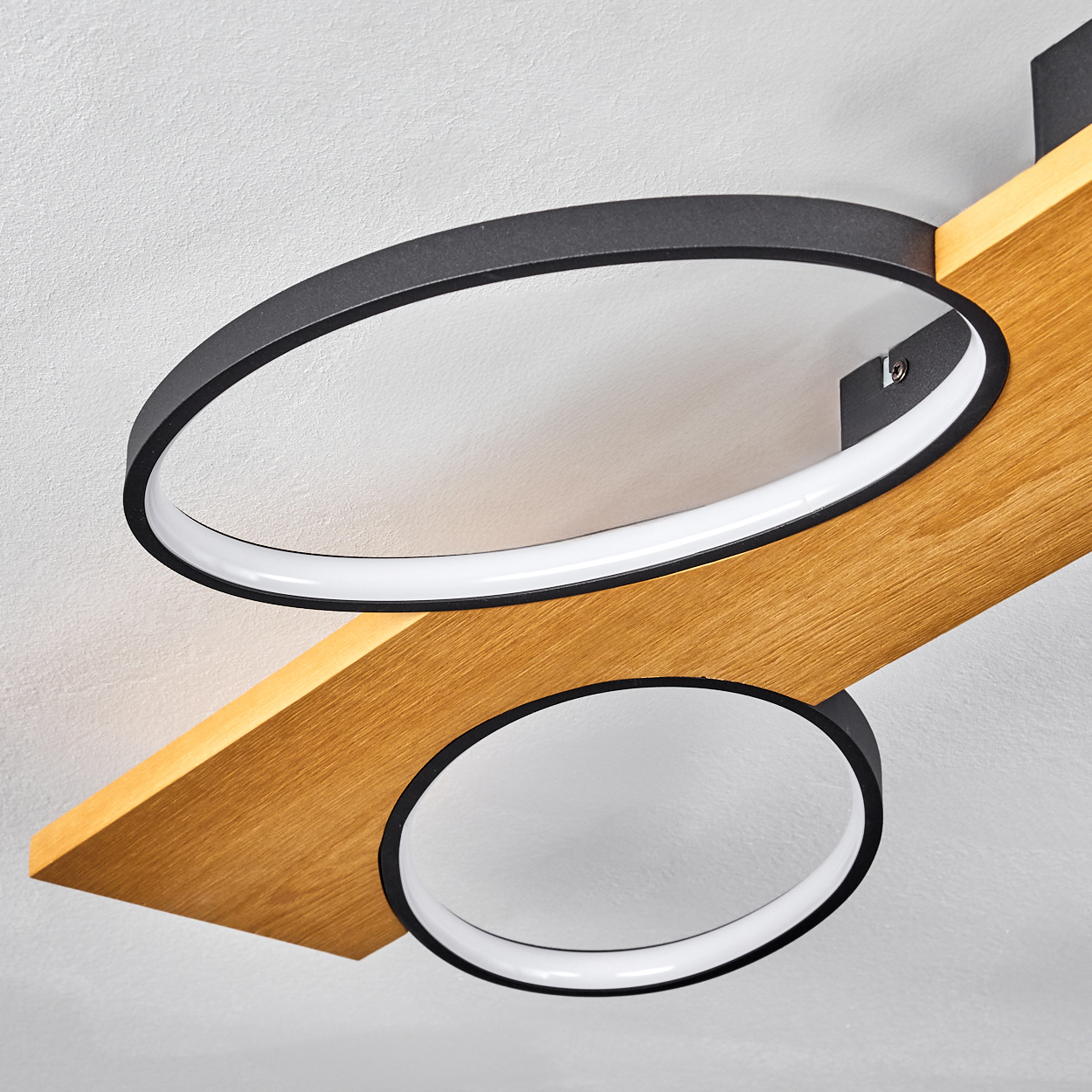 Moderne Deckenlampe mit zwei schwarzen und weißen kreisförmigen Lichtern an einem Holzbalken, an einer weißen Decke befestigt.