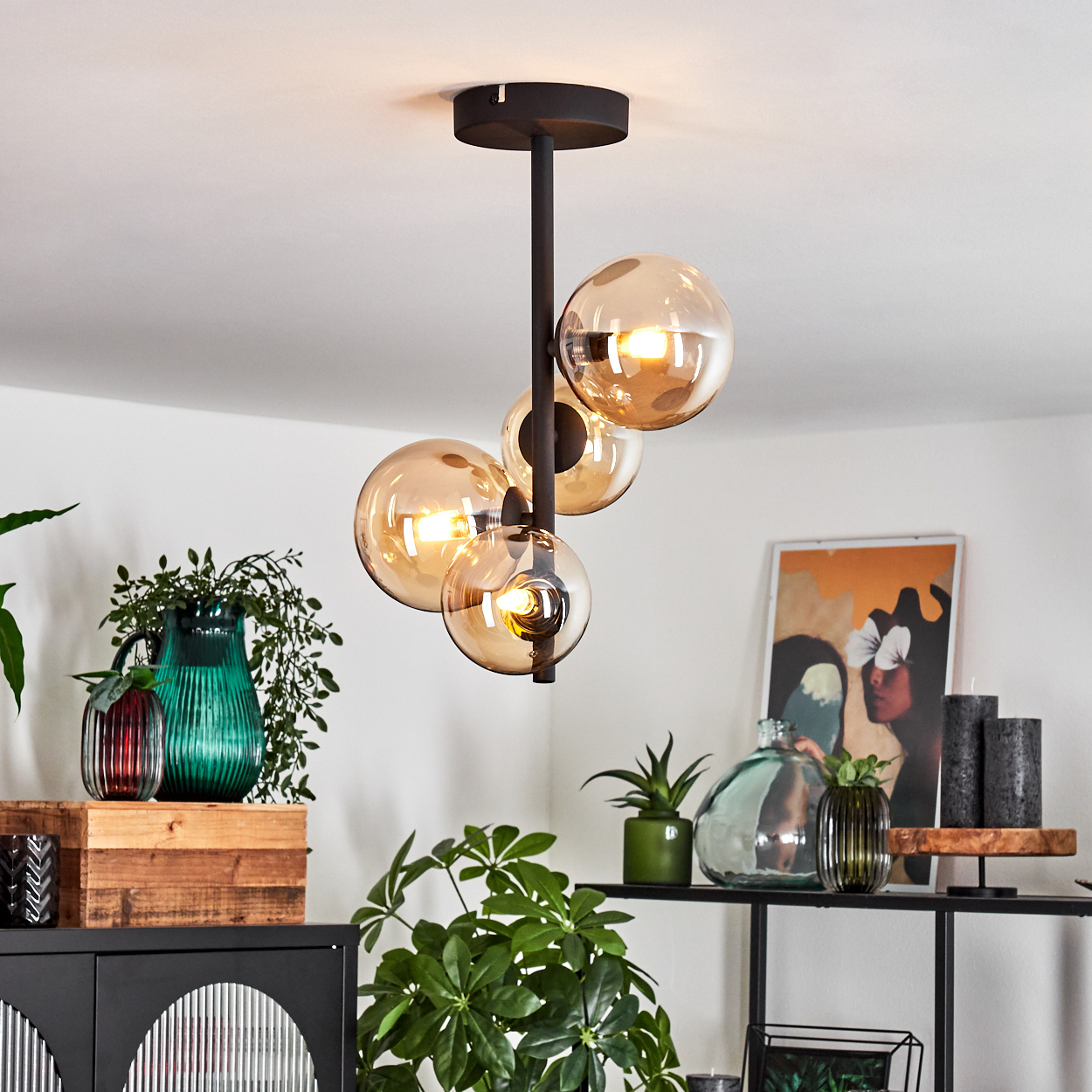 Eine moderne Deckenlampe mit vier bernsteinfarbenen Glaskugeln. Der Raum hat Pflanzen, Kunst und Dekorationsartikel auf Regalen.