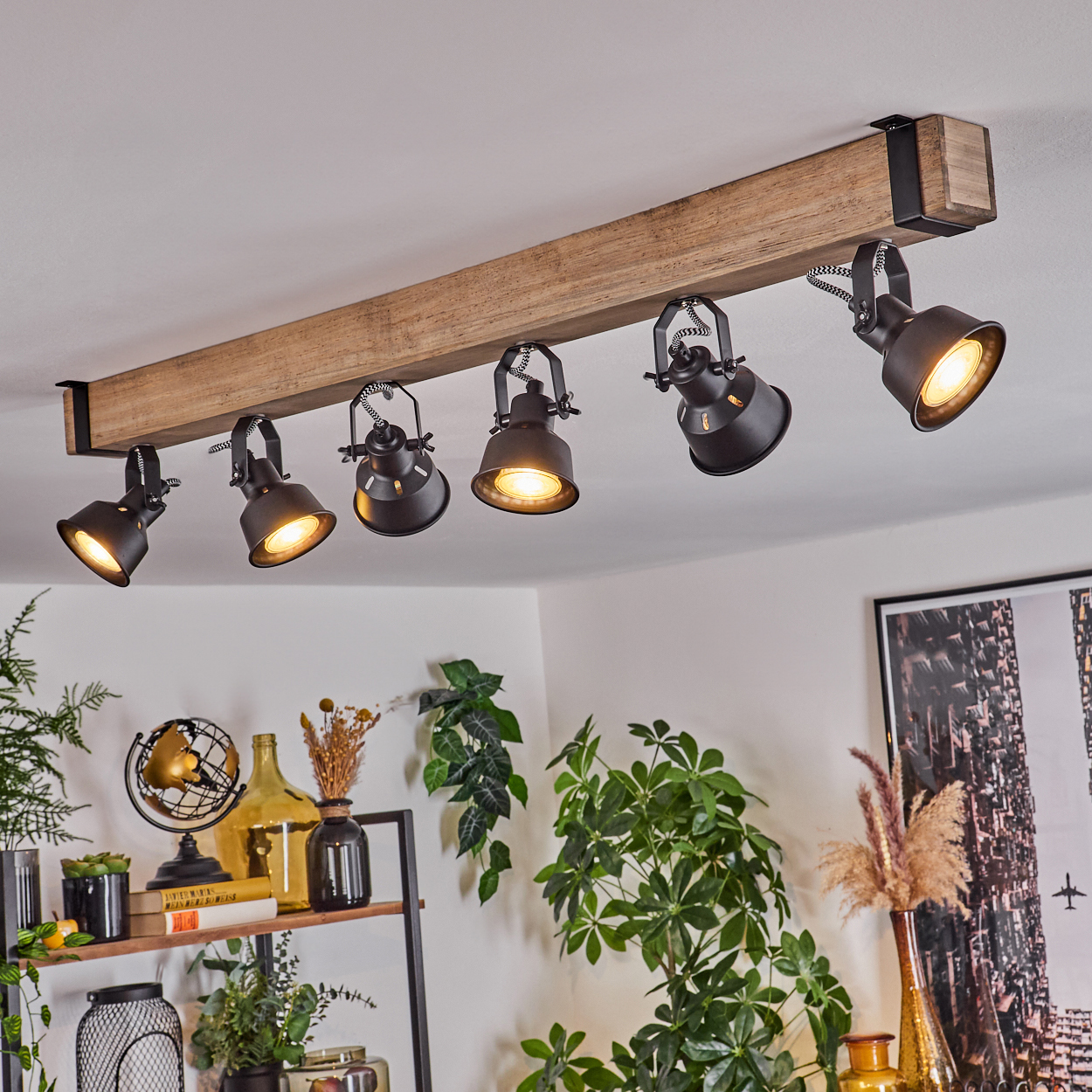 Deckenstrahler an Holzbalken. Dekorative Pflanzen, Globus und Flaschen stehen auf einem Regal. Rechts ein gerahmtes Bild.