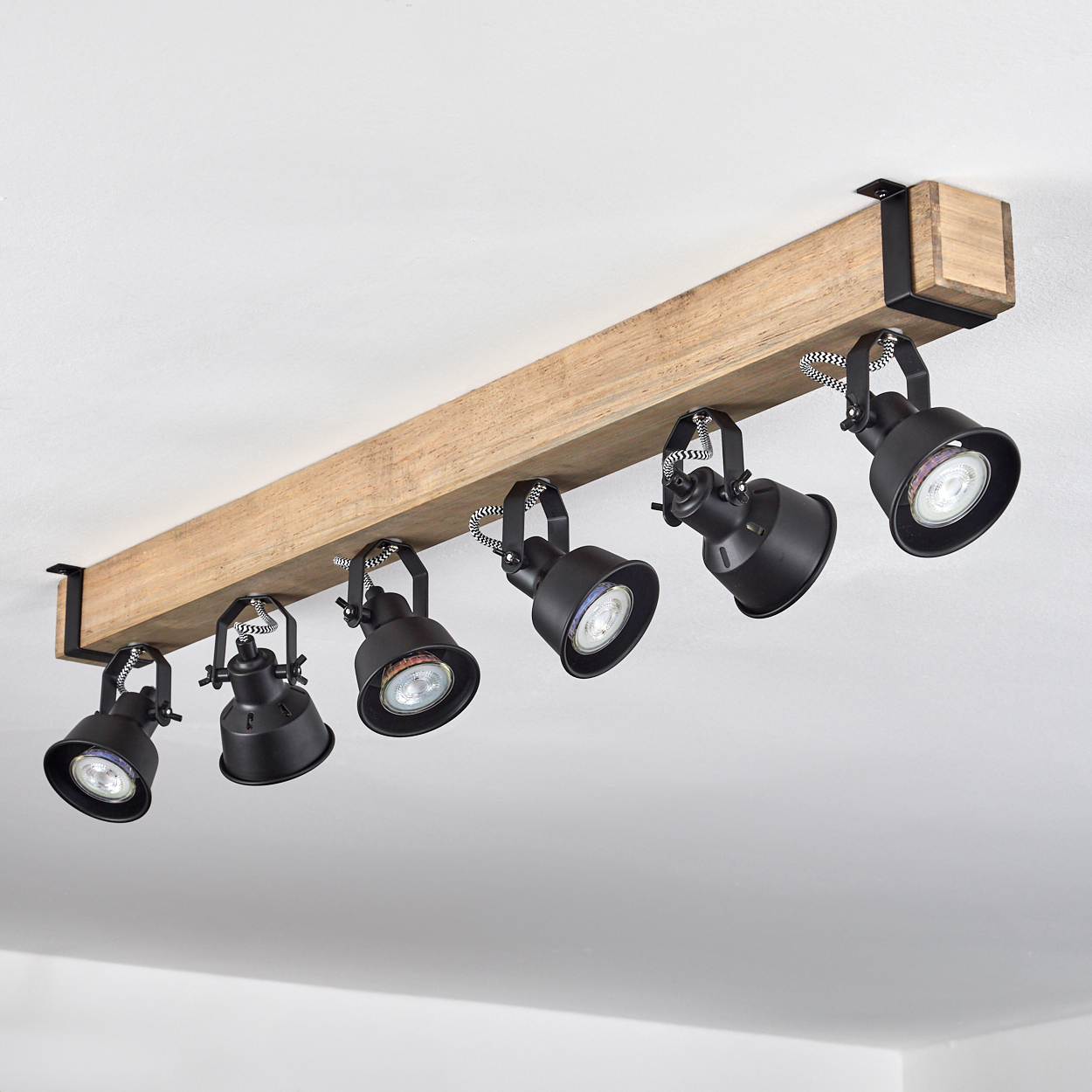 Ein Holzbalken mit sechs schwarzen Strahlern. Die Lichter zeigen nach unten. Der Hintergrund ist eine weiße Decke.