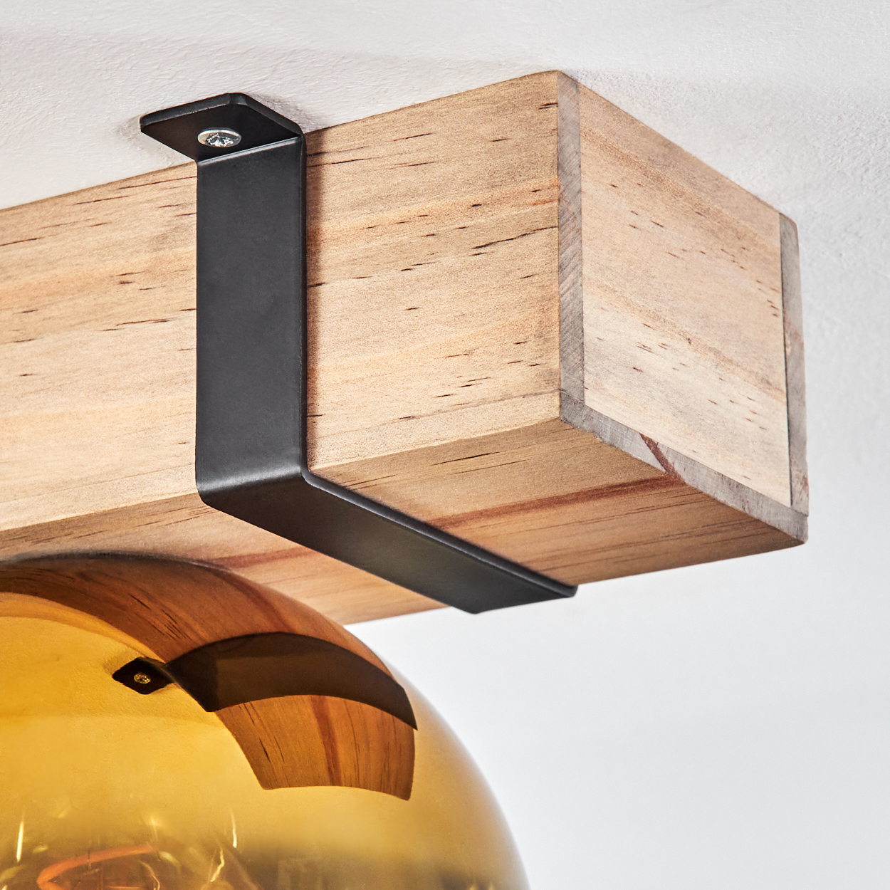 Holzbalken, gehalten von schwarzen Metallbügeln, mit einem goldenen Glasschirm darunter. Vor weißem Hintergrund.