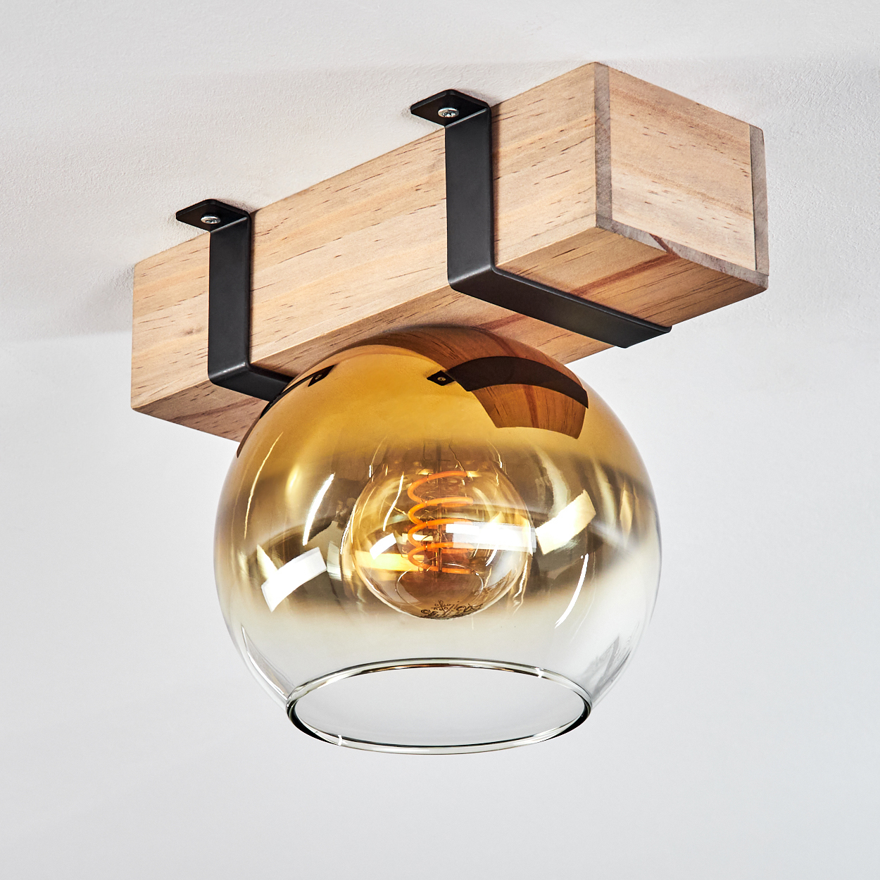 Eine Leuchte mit Holzbalken und Glasschirm. Der Schirm ist bernsteinfarben, die Glühbirne ist sichtbar.