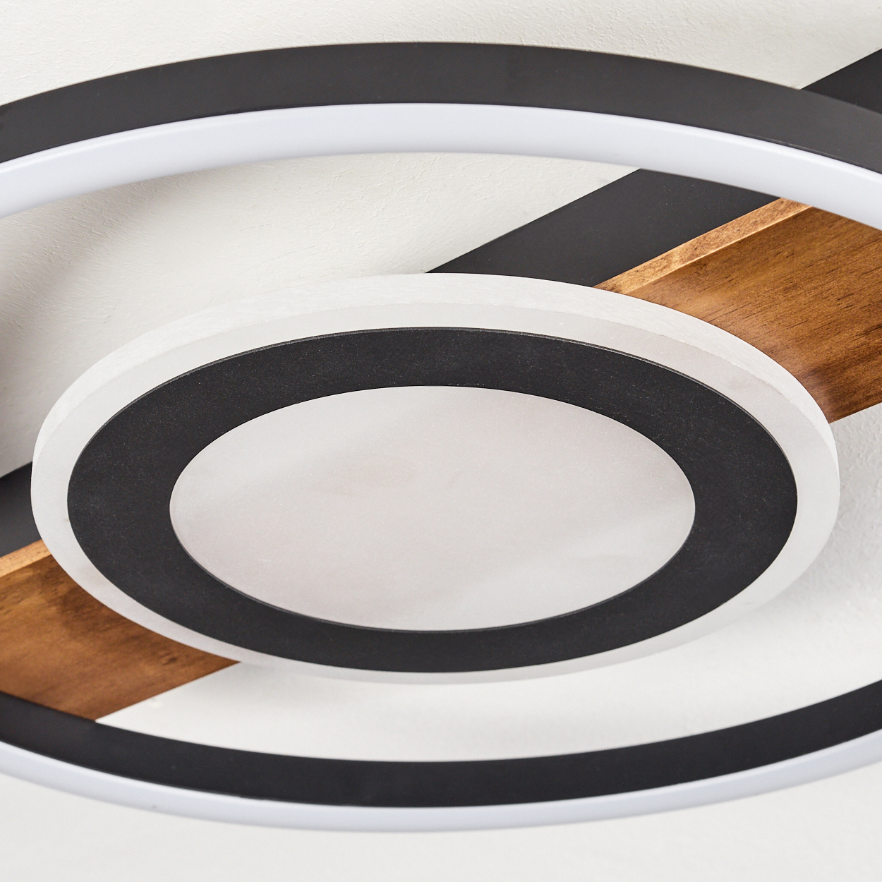 Deckenleuchte mit schwarzen, weißen und Holzelementen. Kreisförmiges Design mit mehreren Ringen und einem zentralen Licht.