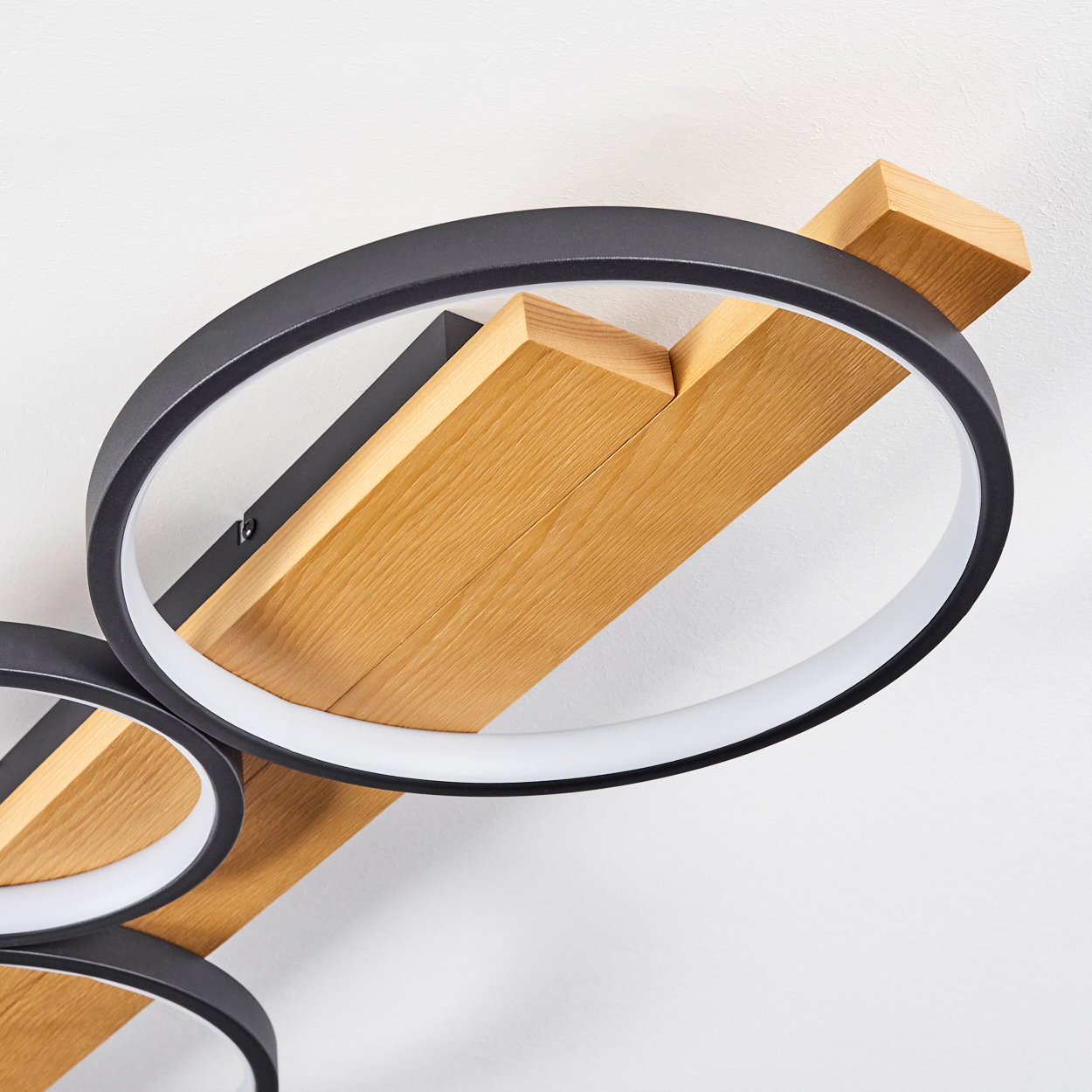 Moderne Deckenleuchte mit schwarzen Ringen und Holzbalken. Weißer Hintergrund. Das Licht besteht aus mehreren miteinander verbundenen Ringen.