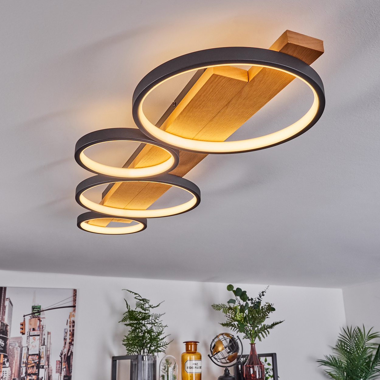 Eine moderne Deckenlampe mit vier kreisförmigen Lichtern. Sie ist vor einer weißen Decke mit Holzbalken angebracht.