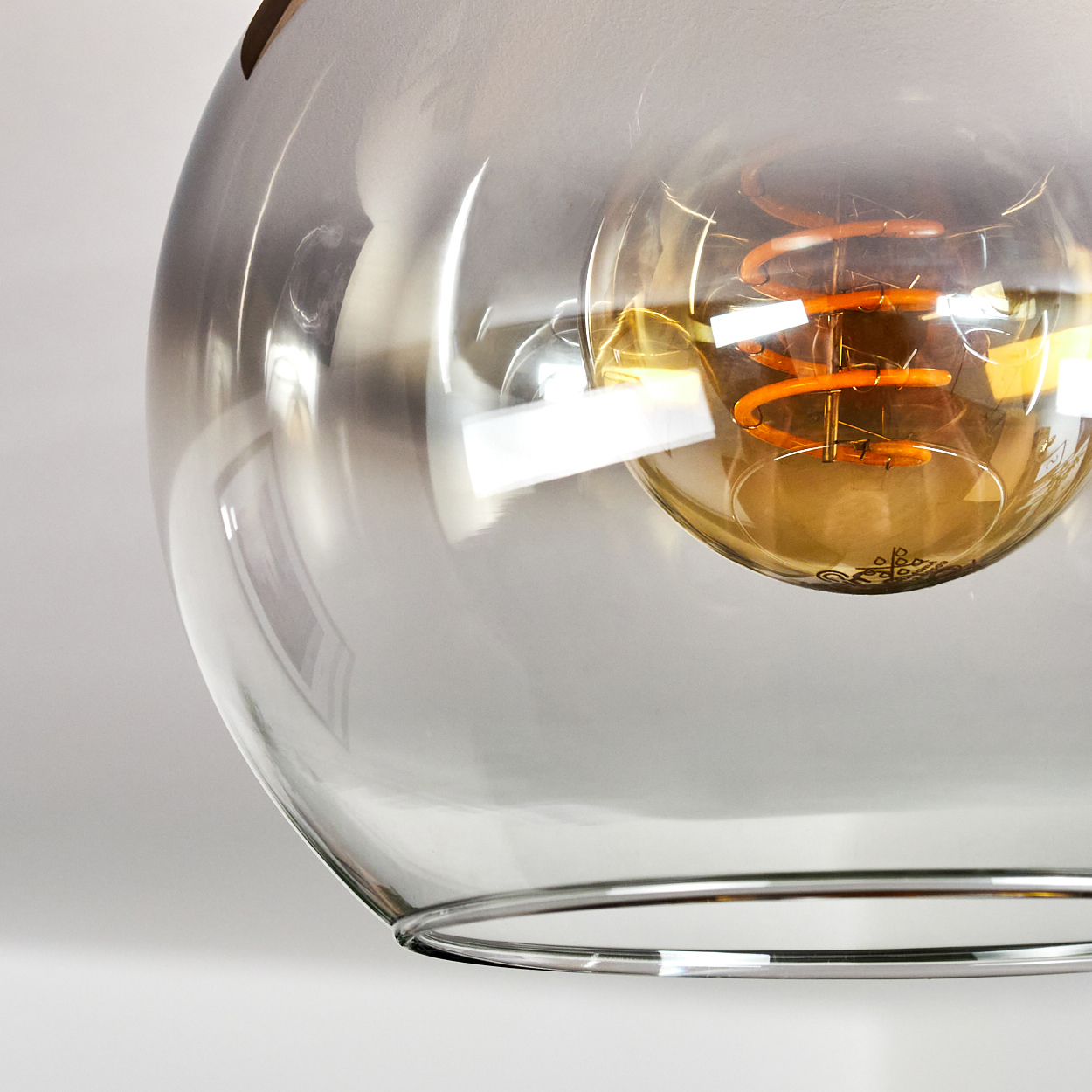 Transparente Glaskugelleuchte mit sichtbarer orangefarbener Glühbirne. Der Hintergrund ist weiß.