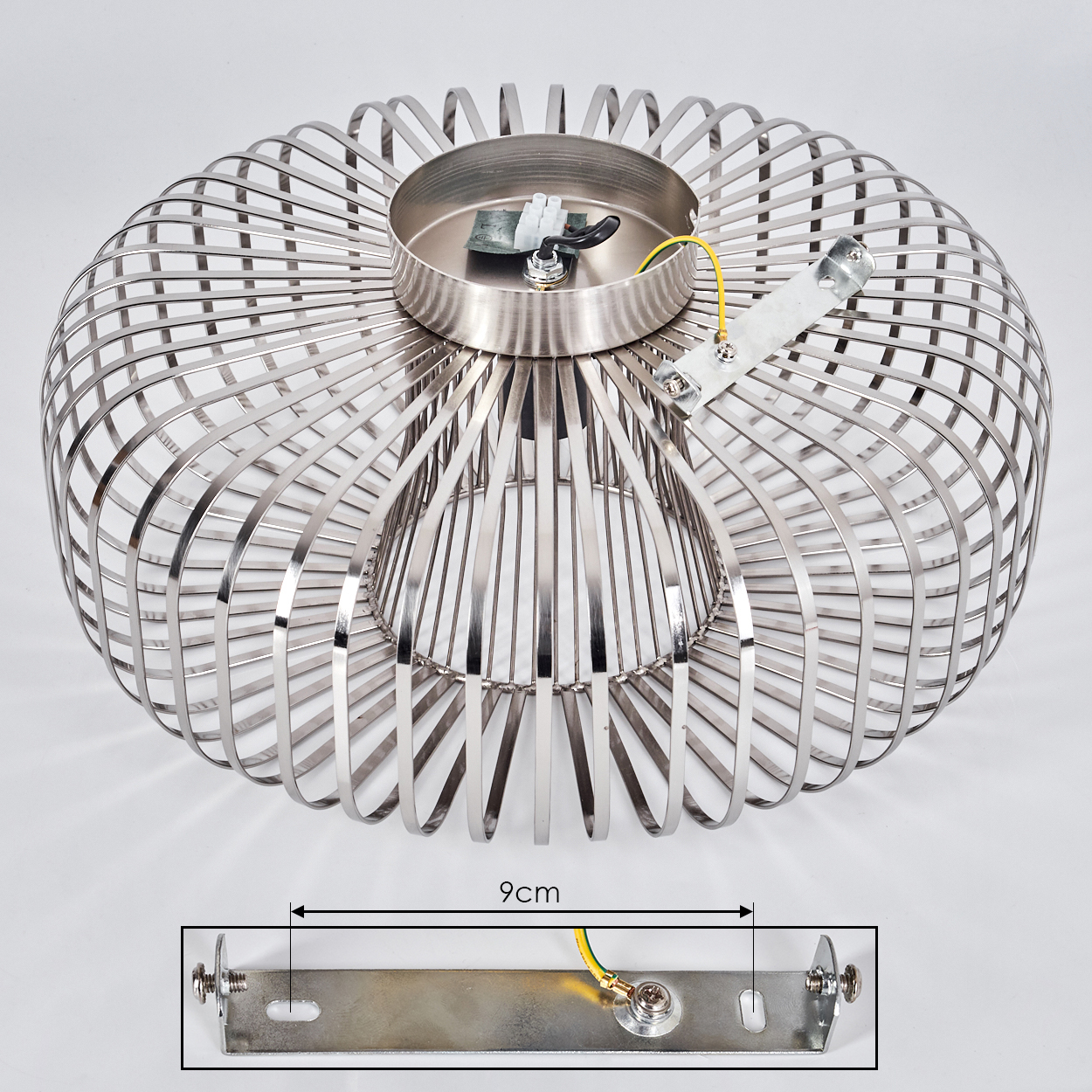 Eine metallische, käfigartige Deckenlampe. Eine Montageplatte mit Drähten ist ebenfalls sichtbar. Die Lampe befindet sich auf einer weißen Oberfläche.