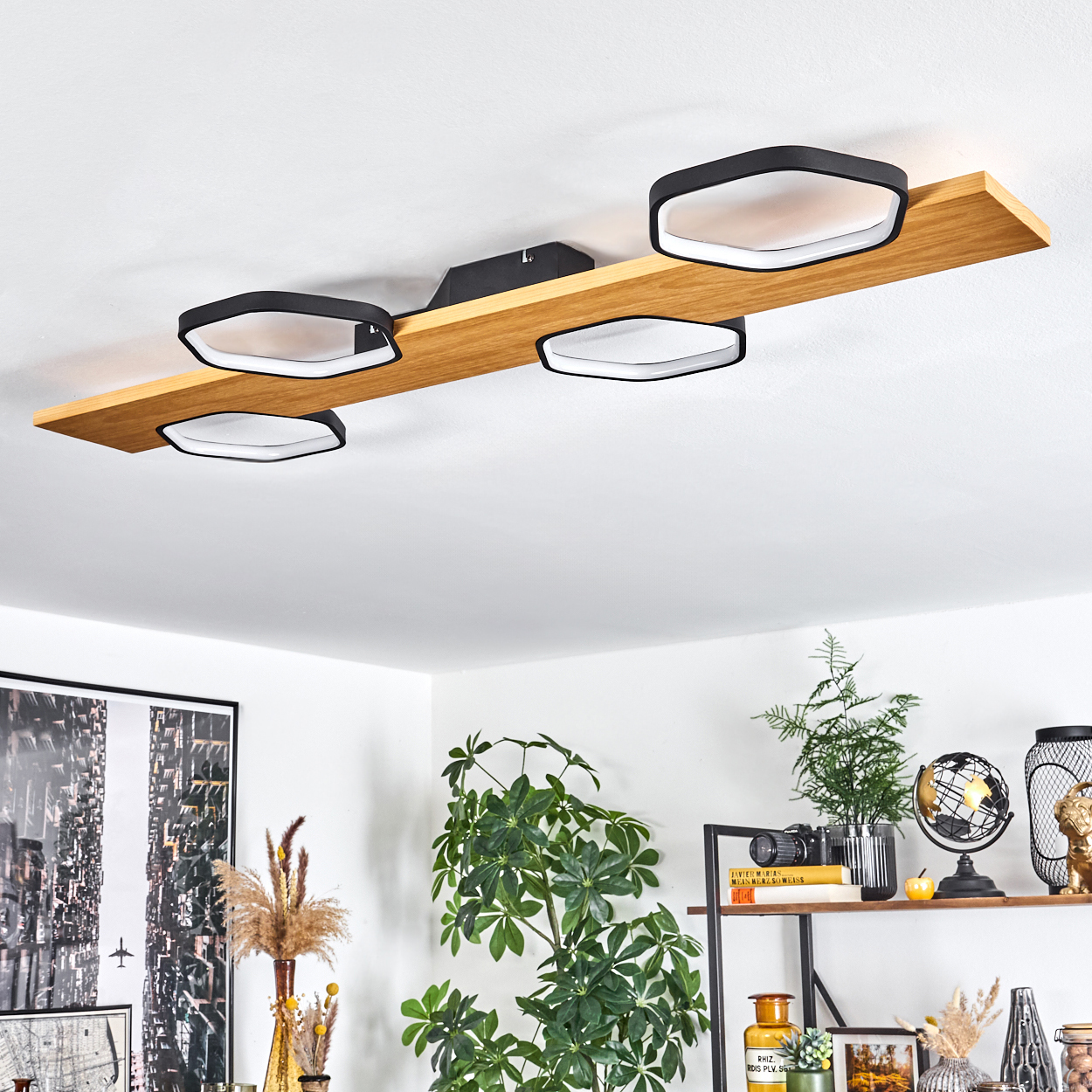 Moderne Deckenleuchte mit vier schwarz gerahmten, weiß beleuchteten sechseckigen Lichtern auf einem Holzbalken. Pflanzen und Dekoration sind unten sichtbar.