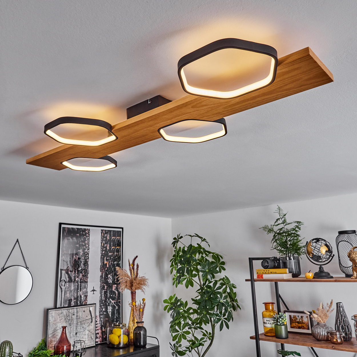Deckenleuchte mit vier schwarzen und weißen sechseckigen Lichtern auf einem Holzbalken. Raum mit Dekor, Pflanzen und einem schwarzen Tisch.