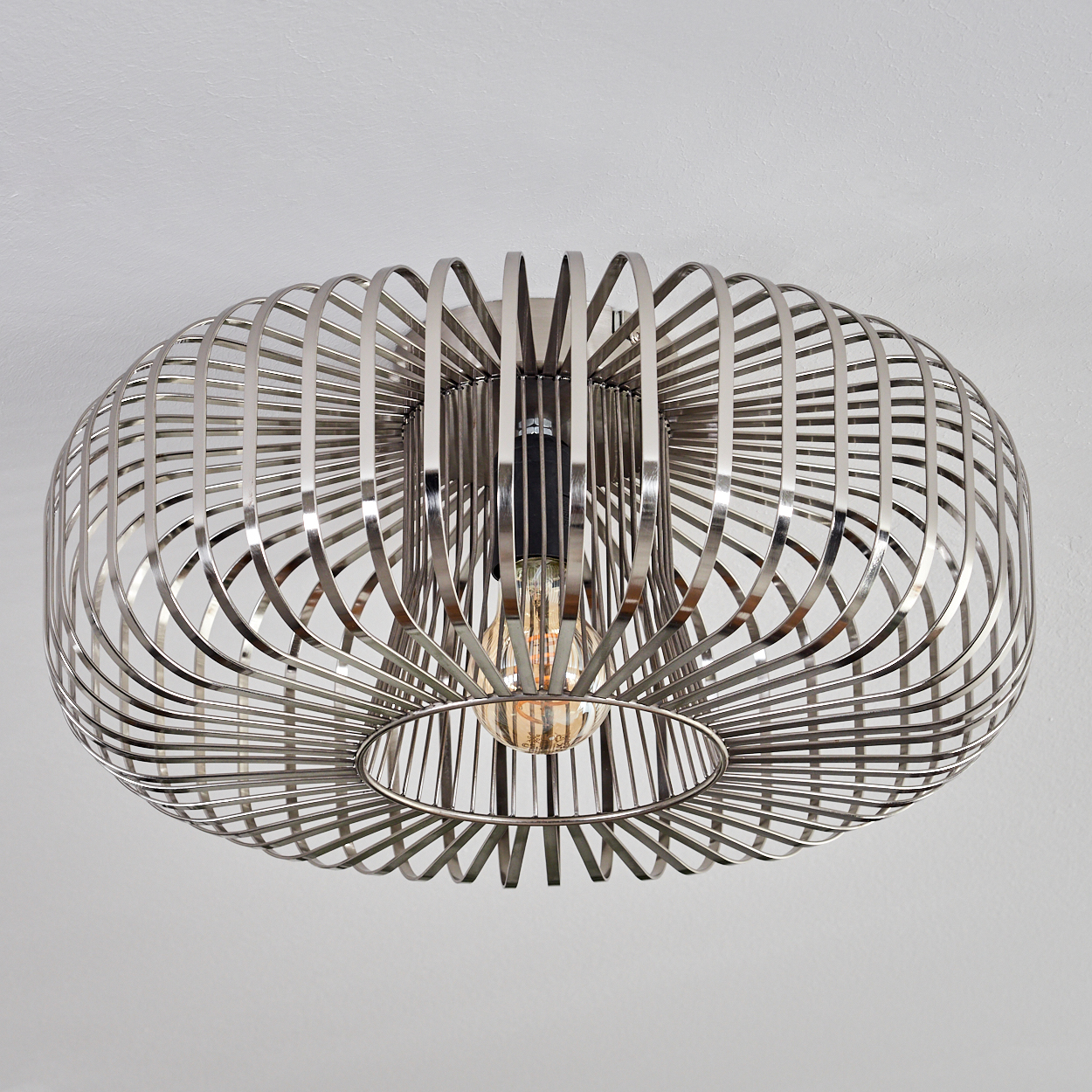 Eine silberne, käfigartige Deckenlampe mit einer Glühbirne im Inneren, die an einer weißen Decke befestigt ist.