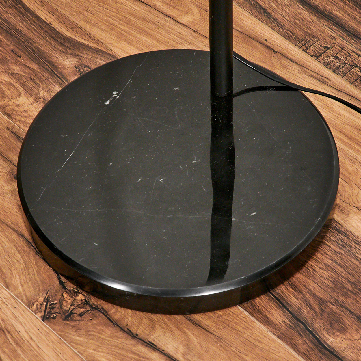 Schwarzer Marmor-Lampensockel auf Holzboden. Eine schwarze Stange ragt aus dem Sockel. Ein schwarzes Kabel verläuft.