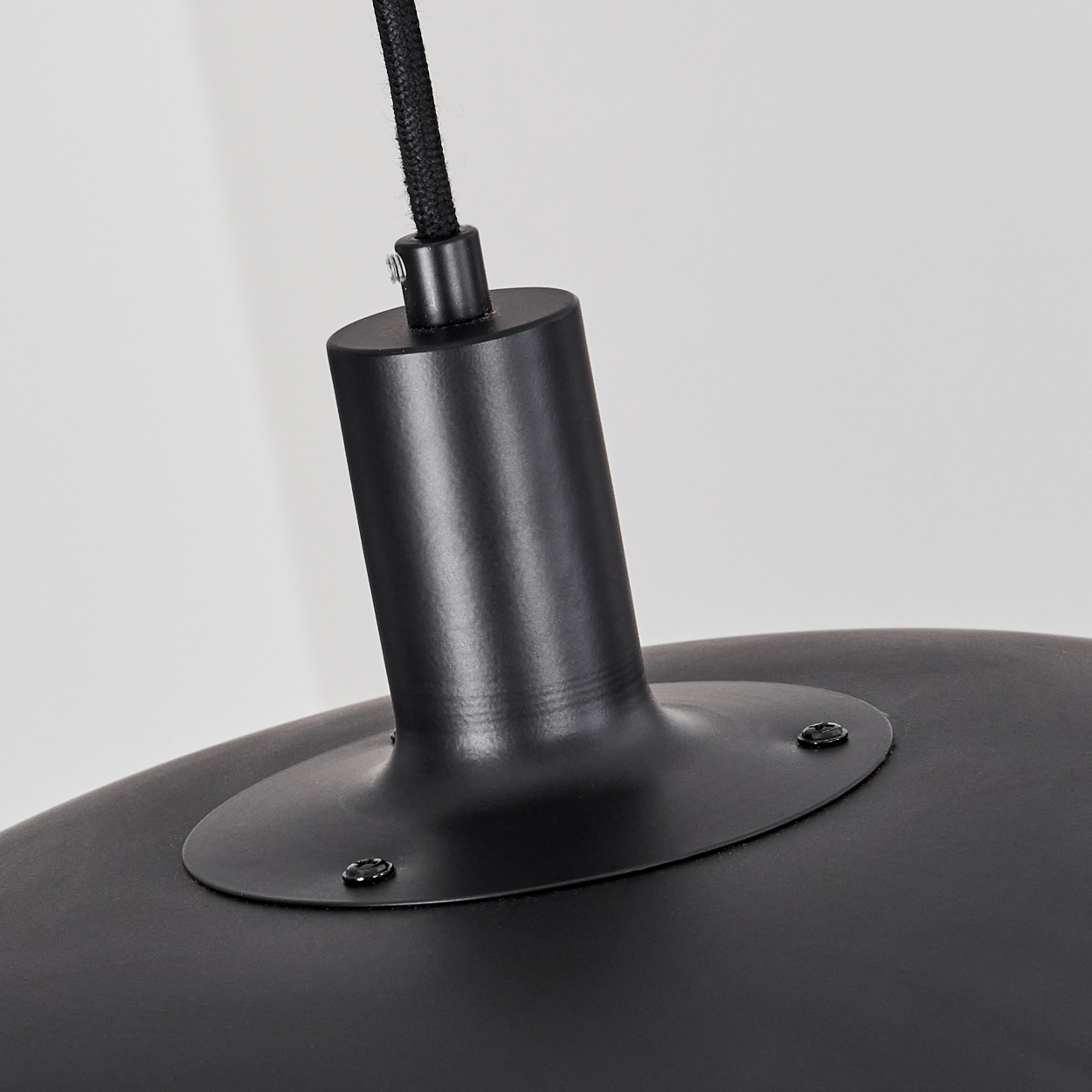 Nahaufnahme einer schwarzen Pendelleuchte. Sie hat ein schwarzes Kabel, eine zylindrische Komponente und einen schalenförmigen Schirm. Der Hintergrund ist weiß.