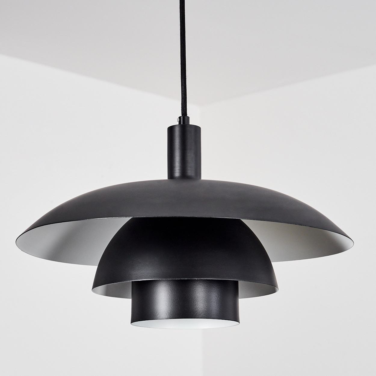 Eine schwarze Pendelleuchte mit mehrschichtigem Design, die an einem schwarzen Kabel hängt. Die Lampe hat einen weißen Innenraum.