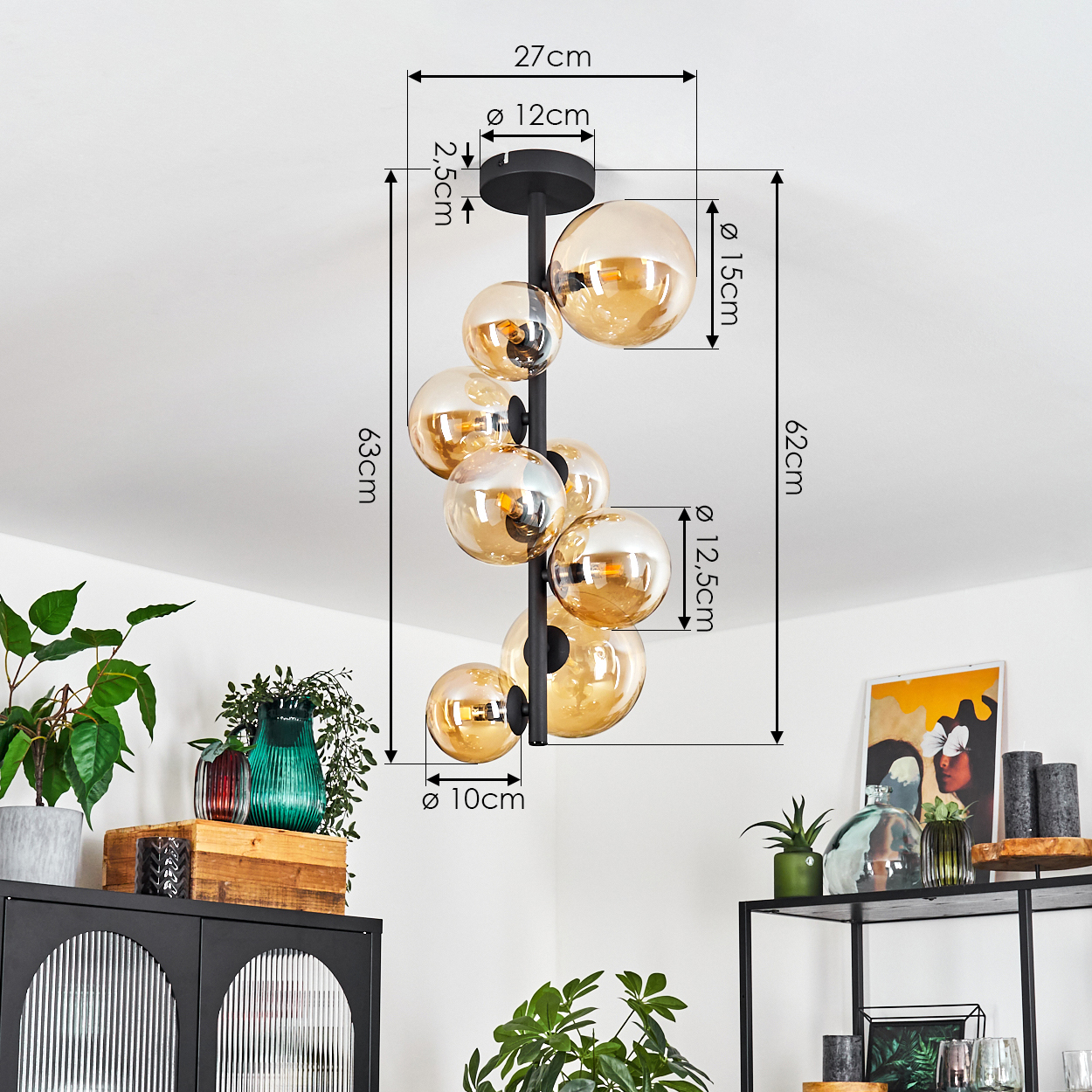 Eine moderne Hängelampe mit bernsteinfarbenen Glaskugeln hängt von der Decke, mit Maßen. Dekorative Gegenstände stehen auf Regalen darunter.