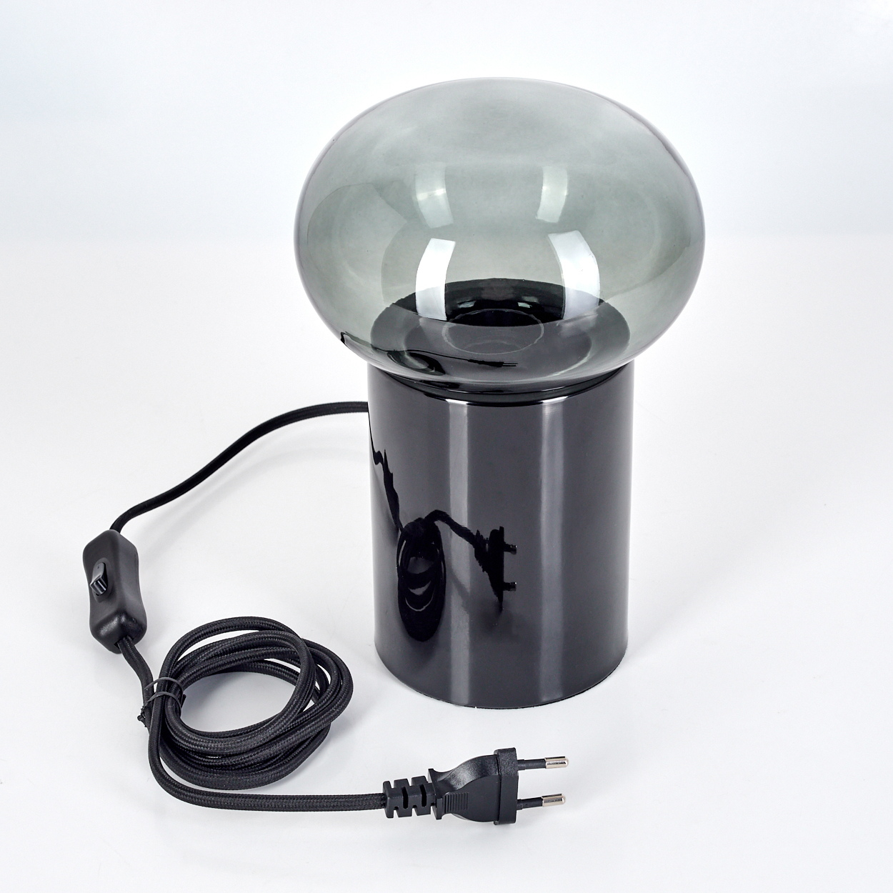 Eine moderne Lampe mit schwarzem Sockel, grauem Glasschirm und schwarzem Netzkabel mit Schalter und Stecker auf weißem Hintergrund.