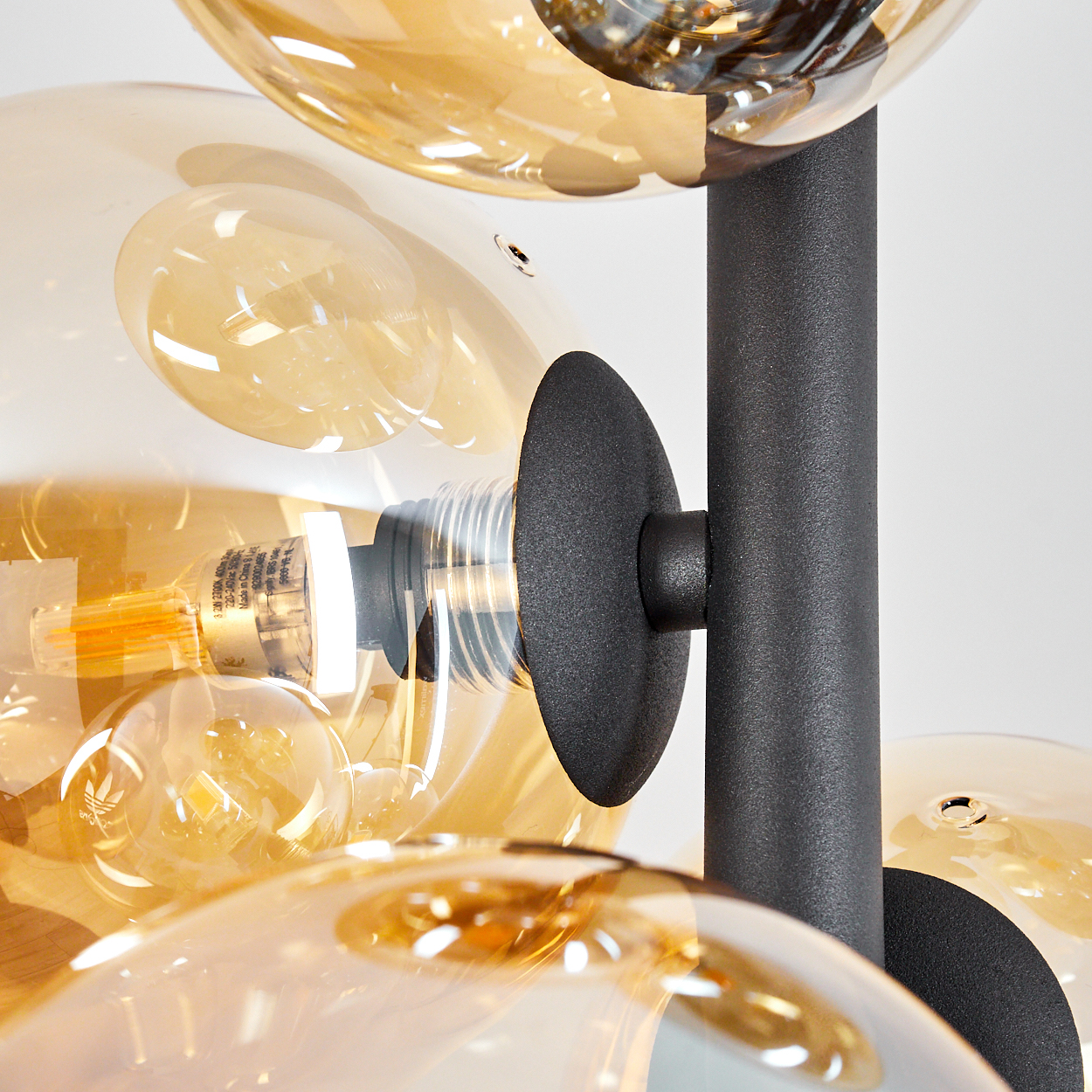 Eine moderne Lampe mit mehreren bernsteinfarbenen Glaskugeln und einem schwarzen Metallrahmen. Die Glühbirnen sind in den Kugeln sichtbar.