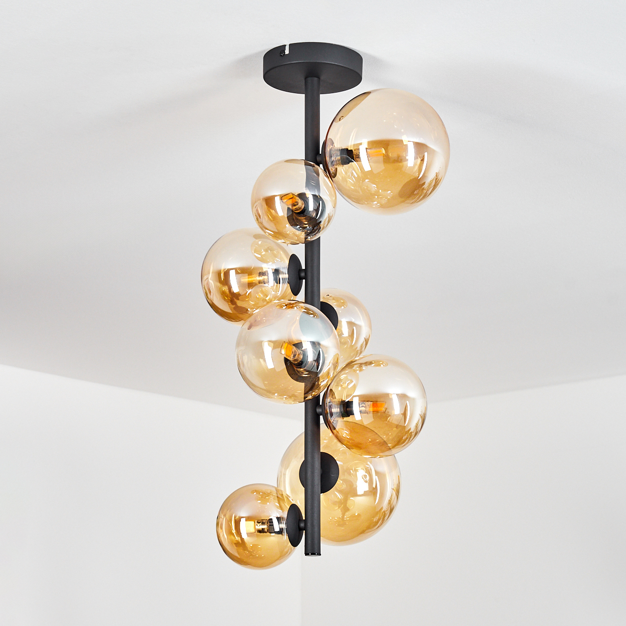 Eine moderne Deckenleuchte mit mehreren bernsteinfarbenen Glaskugeln. Sie hängt an einer schwarzen Metallstange von der Decke.