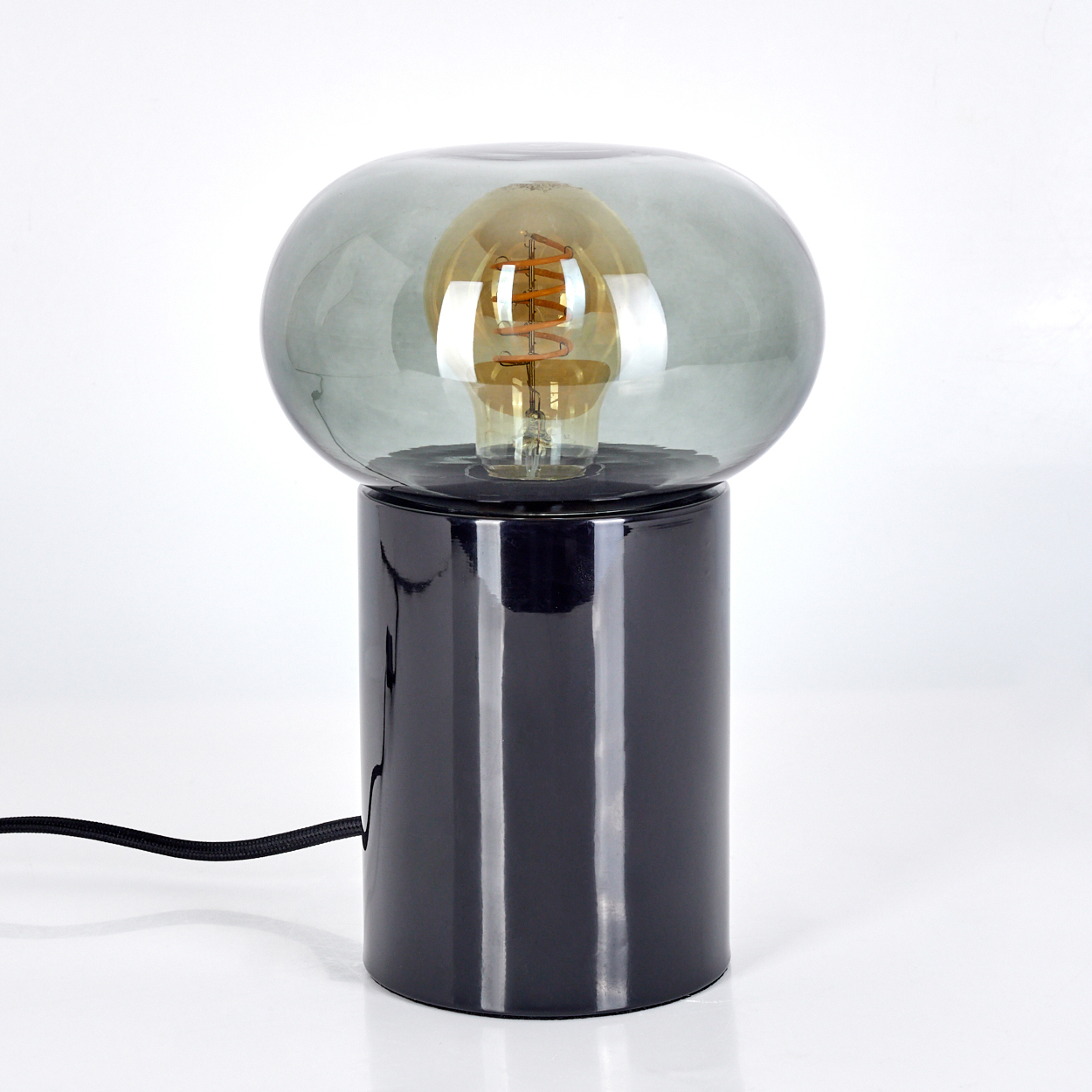 Eine schwarze Lampe mit einem grauen Glaskolben und einer sichtbaren Glühbirne. Die Lampe steht auf einer weißen Oberfläche.