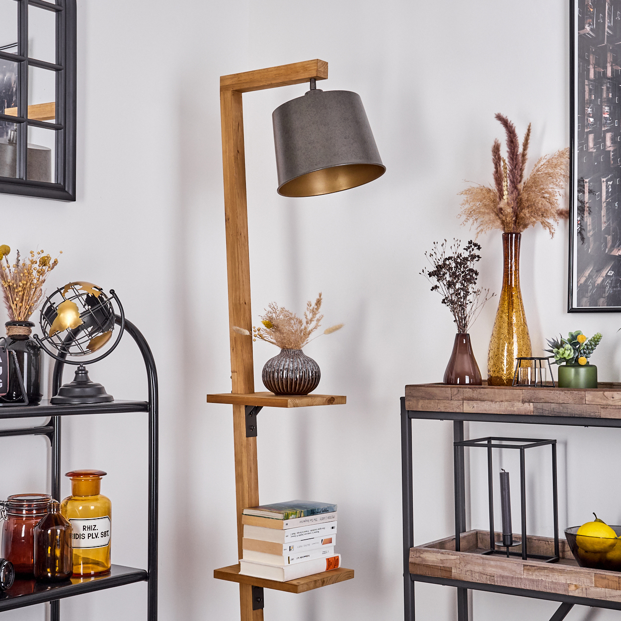 Eine hölzerne Stehlampe mit grauem Lampenschirm. Regale beherbergen Vasen, Bücher und Dekorationen. Ein schwarzes Metallregal zeigt weitere Artikel.