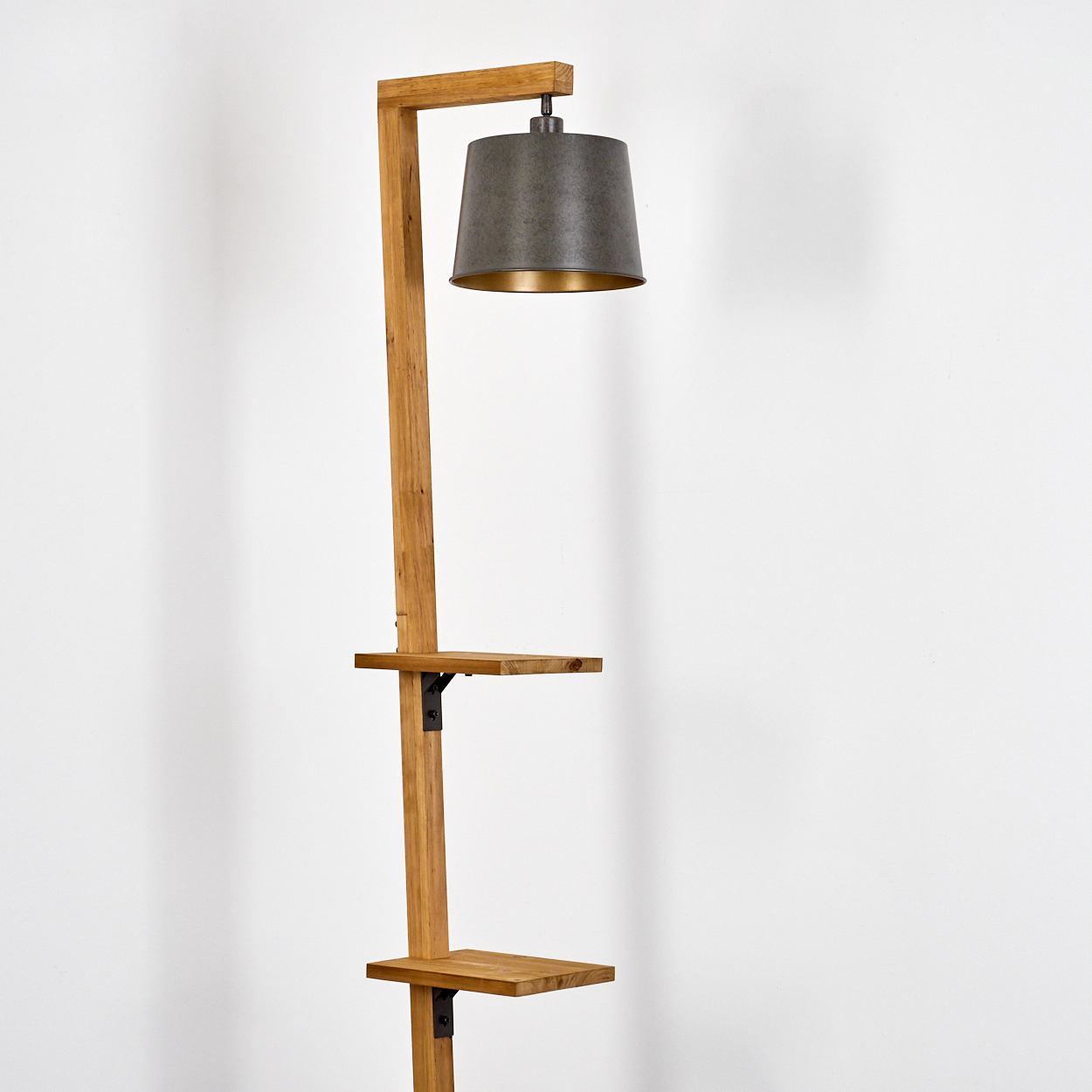 Eine Stehlampe aus Holz mit grauem Lampenschirm und zwei Regalen. Der Hintergrund ist eine weiße Wand.