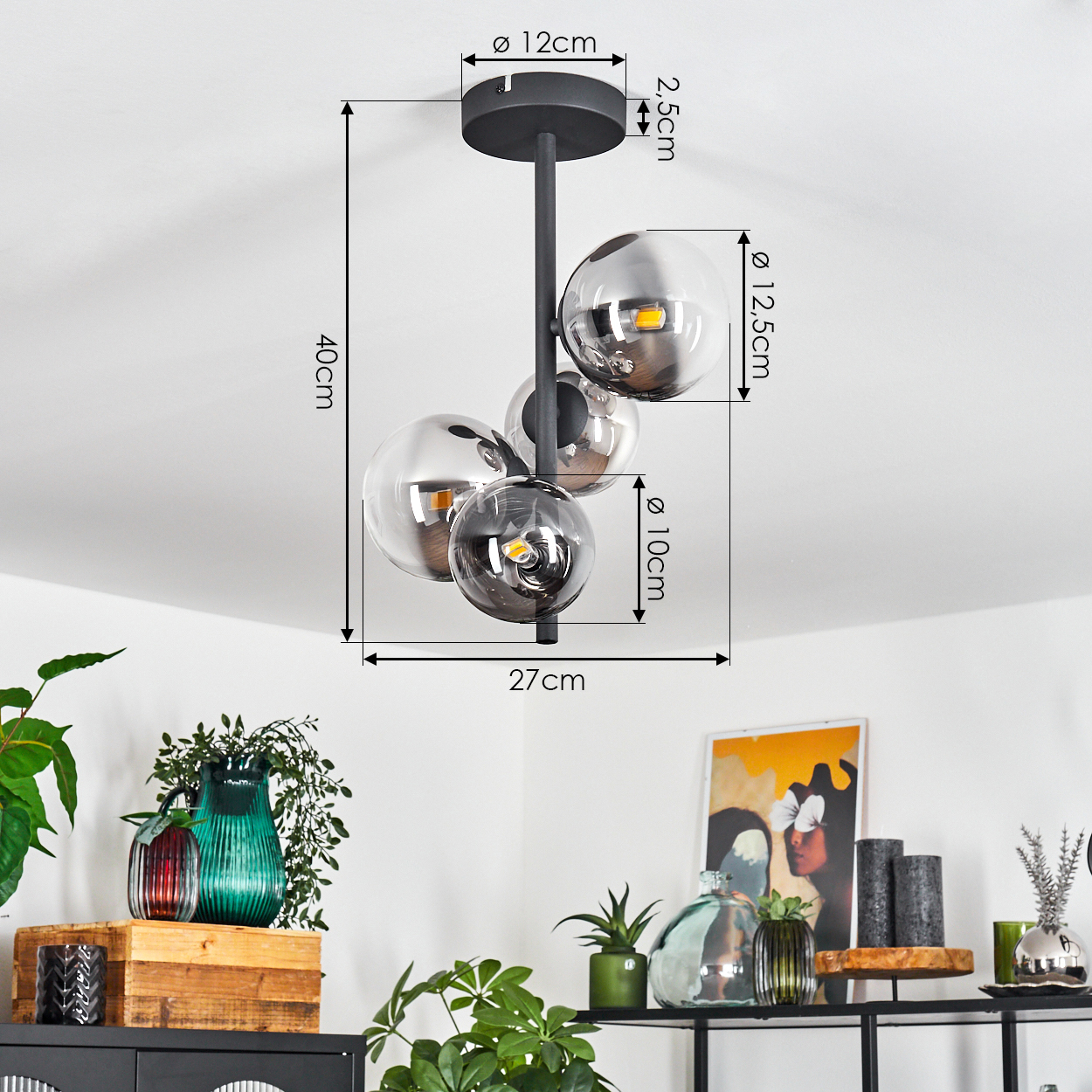 Eine moderne Deckenlampe mit vier kugelförmigen Glasschirmen, Maße markiert. Darunter ein Regal mit Vasen, Pflanzen und einem gerahmten Kunstwerk.