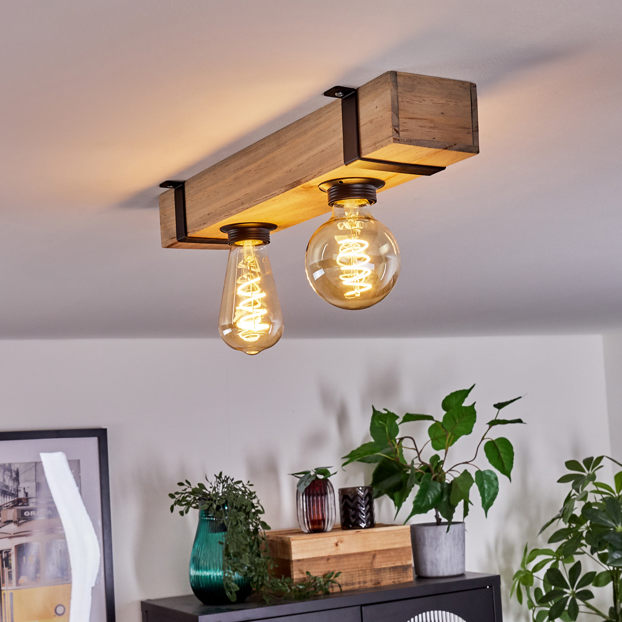 Eine hölzerne Deckenleuchte mit zwei Edison-Glühbirnen. Darunter ein Schrank mit Pflanzen und Dekorationsartikeln.