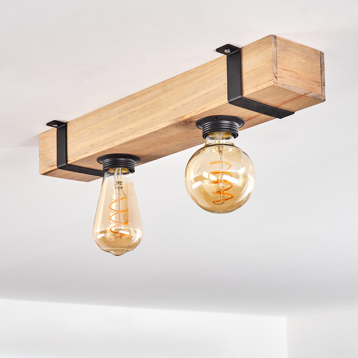 Eine Deckenleuchte mit Holzbalken und zwei Edison-Glühbirnen. Der Balken ist hellbraun, mit schwarzen Metallbügeln. Die Glühbirnen sind bernsteinfarben.
