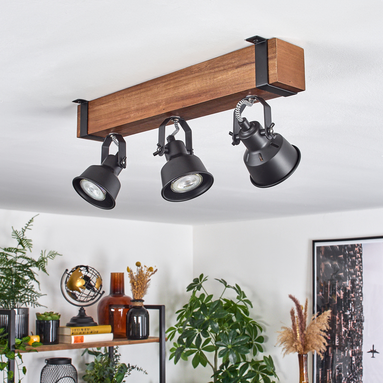 Drei schwarze Scheinwerfer an einem Holzbalken. Die Lichter sind nach unten gerichtet. Pflanzen und Dekorationsartikel befinden sich darunter.