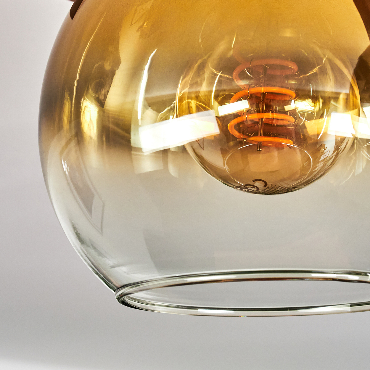 Nahaufnahme einer Glashängeleuchte. Die Glühbirne befindet sich in einer transparenten Glaskugel. Der Glühfaden ist orange.