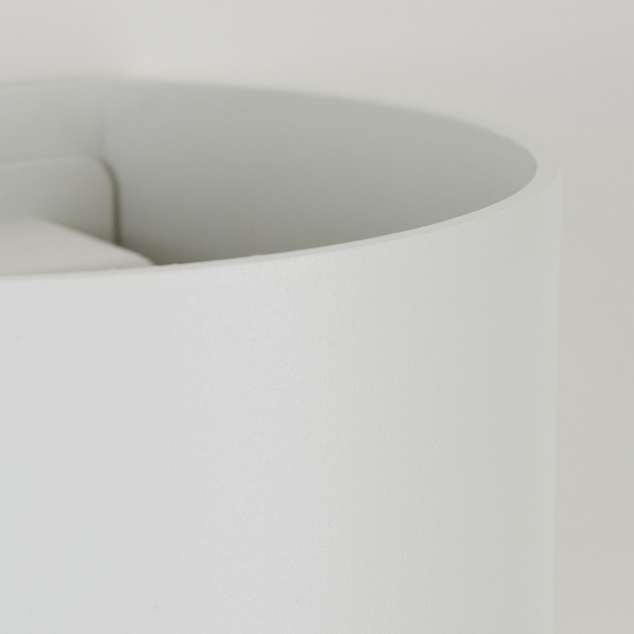 Nahaufnahme eines weißen, gebogenen Objekts vor weißem Hintergrund. Die Textur des Objekts ist leicht rau. Die Szene ist minimalistisch.