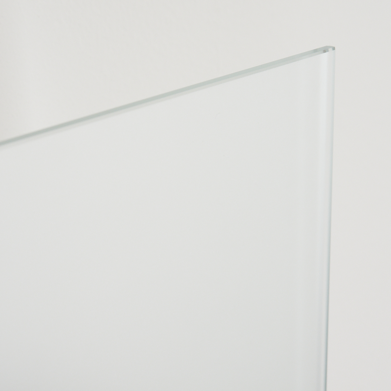 Nahaufnahme einer transparenten Glasscheibe vor weißem Hintergrund. Die Kante der Scheibe ist sichtbar und reflektiert Licht.