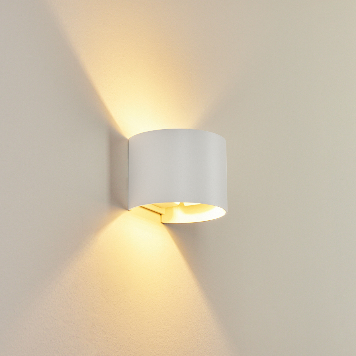 Eine weiße Wandleuchte an einer beigefarbenen Wand. Das Licht scheint nach unten und erzeugt Schatten.