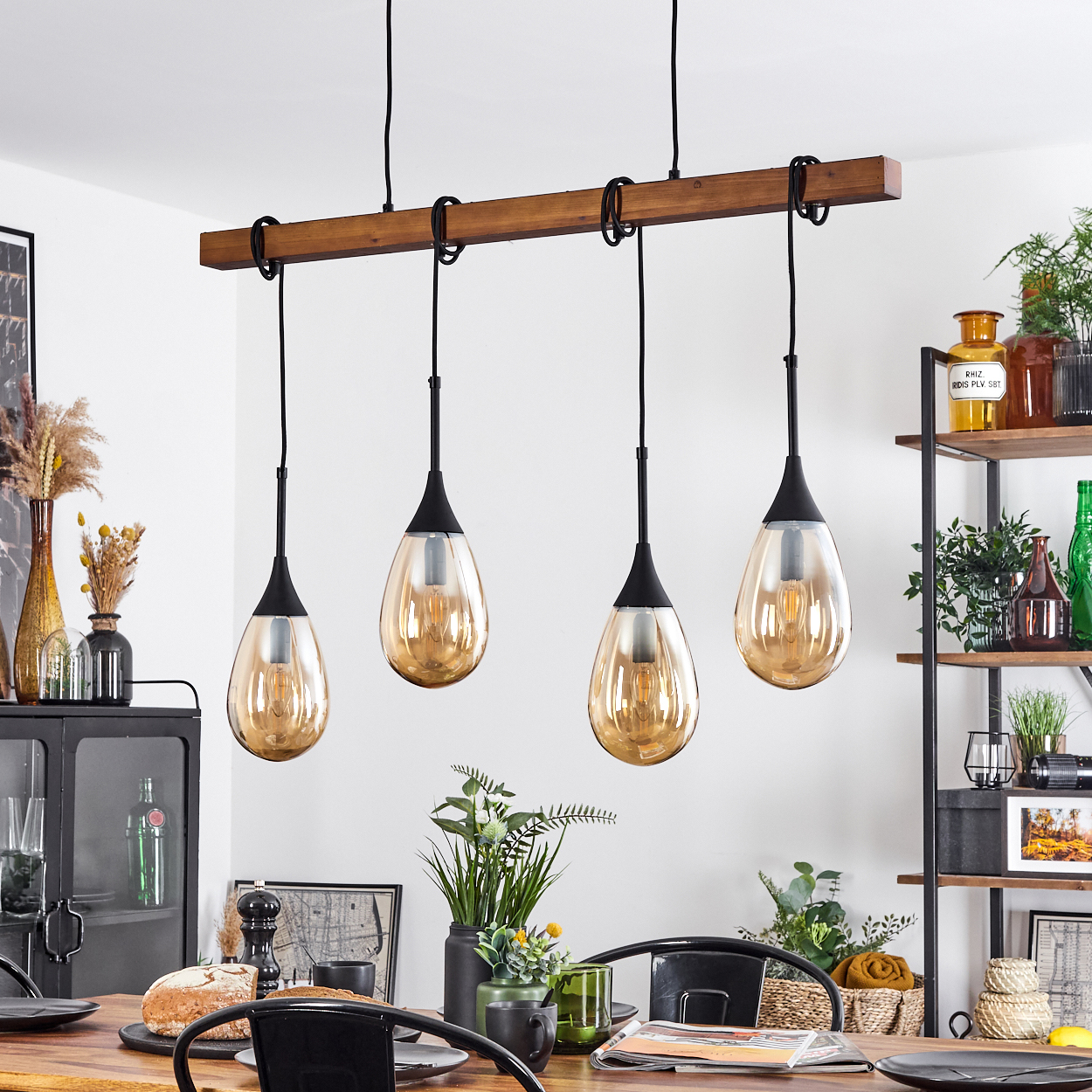 Esszimmer mit Holztisch. Vier Hängelampen. Regale mit Pflanzen und Dekorationen. Schwarze Stühle.