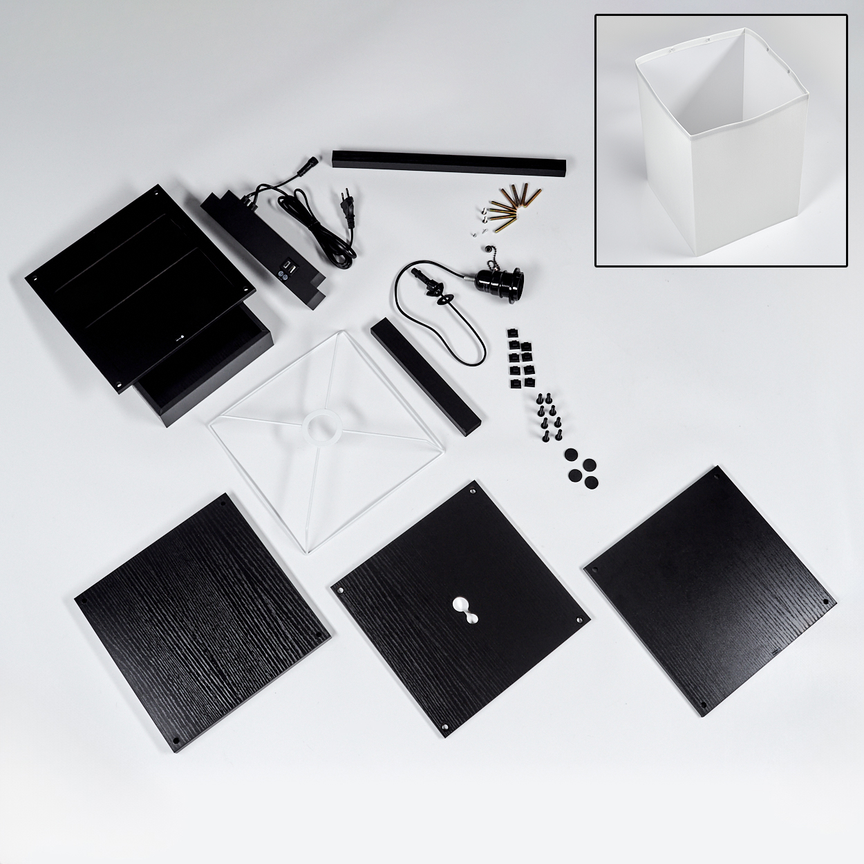 Draufsicht auf Lampenteile. Schwarze Quadrate und rechteckige Teile, weißer Lampenschirm, Schrauben und Drähte liegen auf weißer Oberfläche.